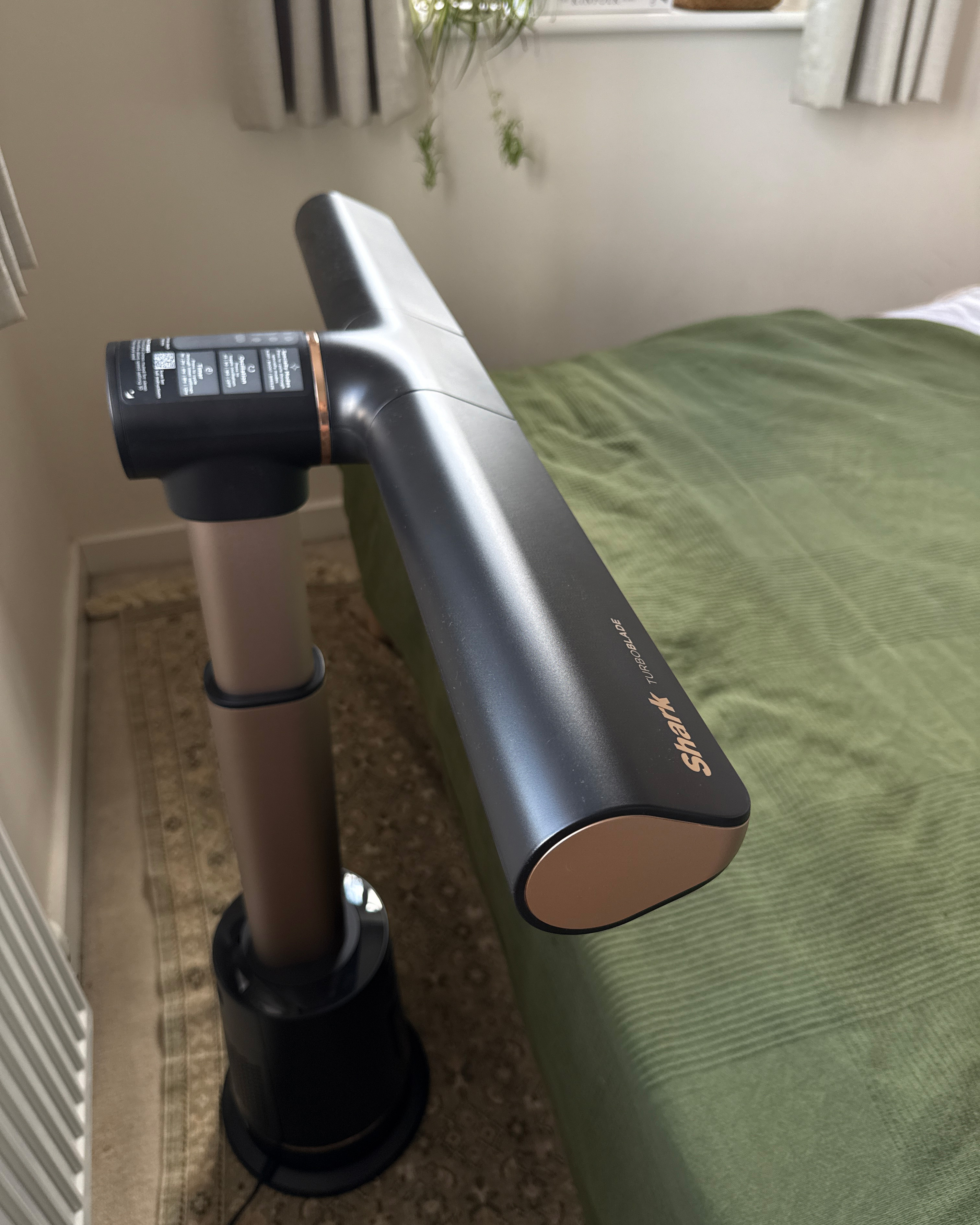 shark turboblade fan at the foot of a bed with a green bedspread in front of a window with grey curtains