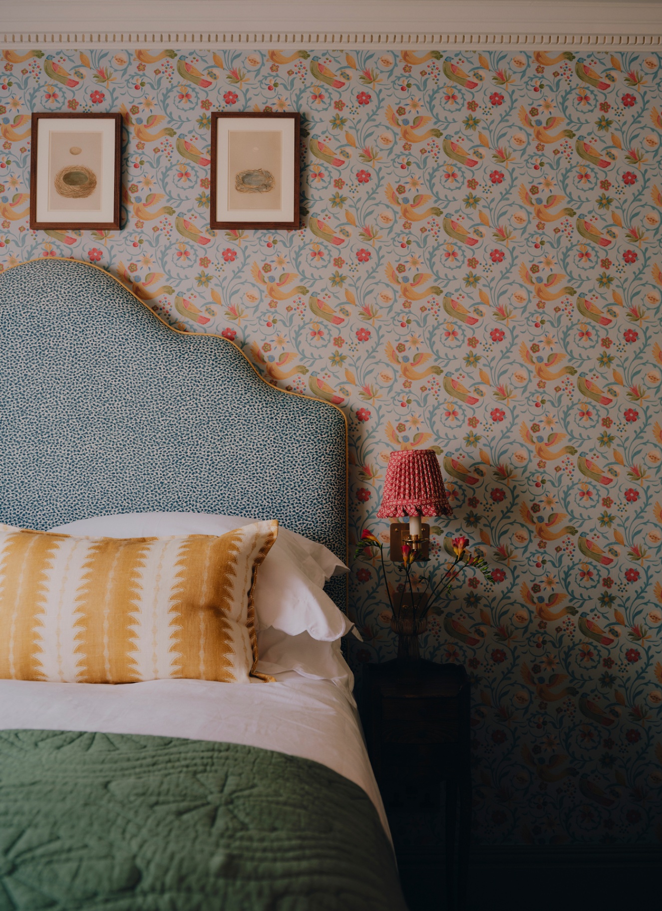 a bed with a blue and white floral headboard, white bedding, a yellow stripe pillow and a green bedspread and a wall covered in blue and yellow floral wallpaper