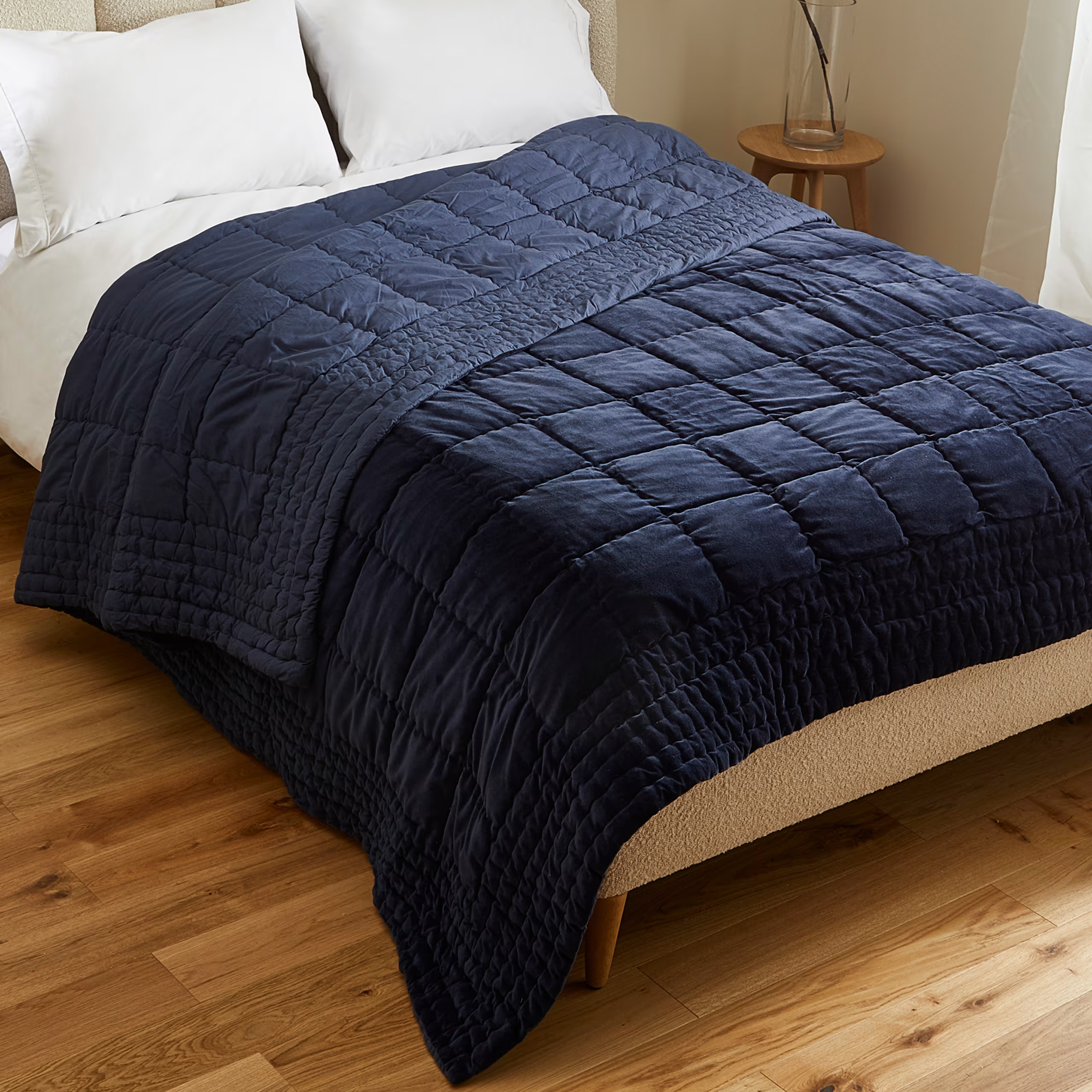 a dark navy velvet quilted bedspread on a white bed and wooden flooring