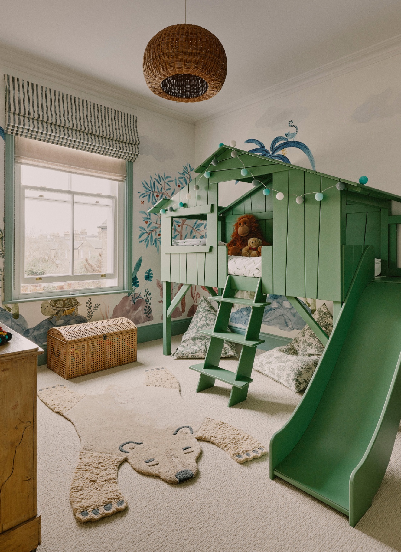 a children's bedroom with a large green wendyhouse bedframe with a slide coming down onto a beige carpet