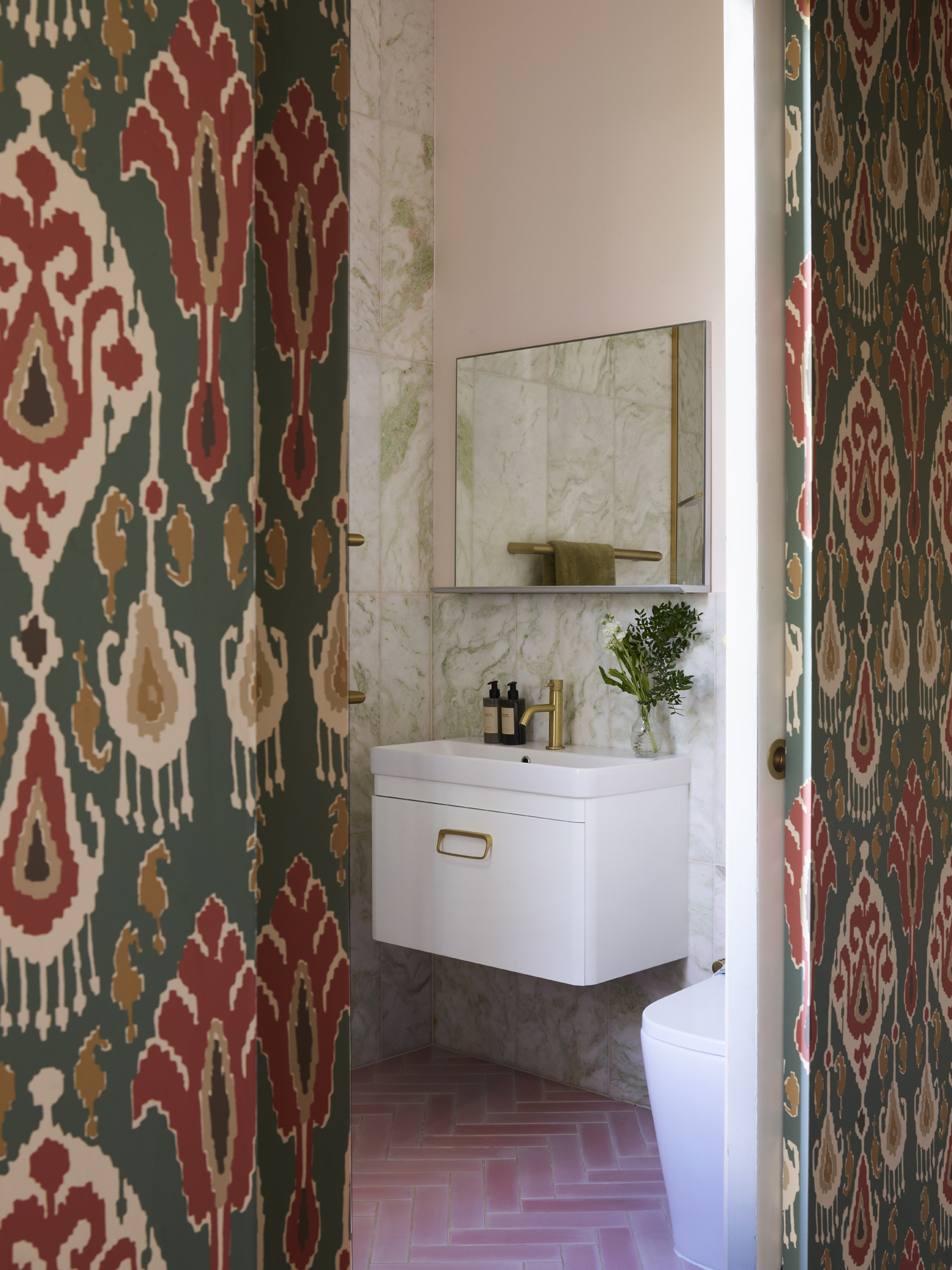 a bathroom pictured with patterned wallpaper, tiled pink herringbone flooring and dusky pink washed walls