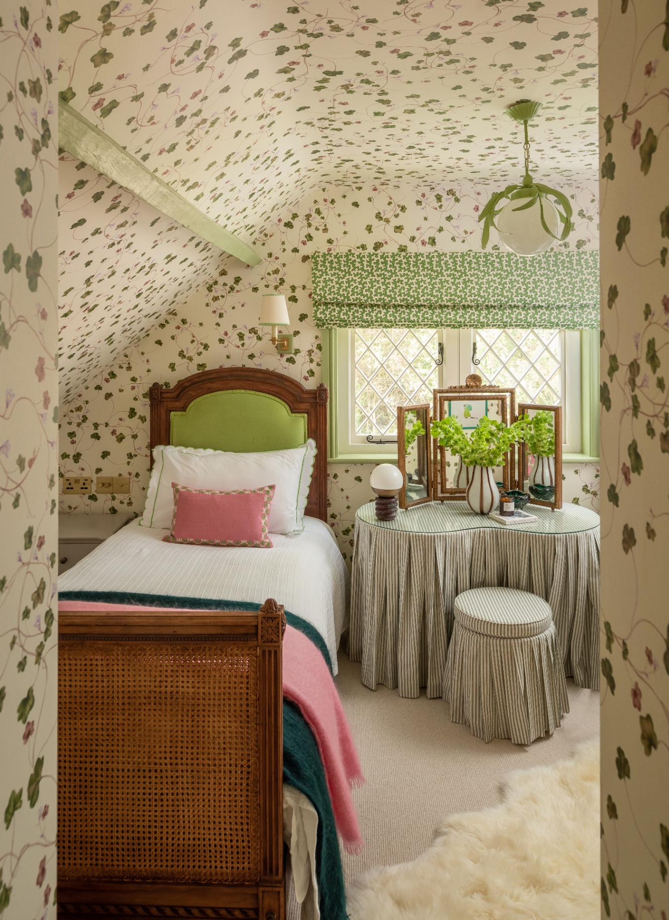 a cottage bedroom with sloping ceilings with cream and green botanical wallpaper drenched on the walls and ceiling and a wooden single bed and a striped textile dressing table