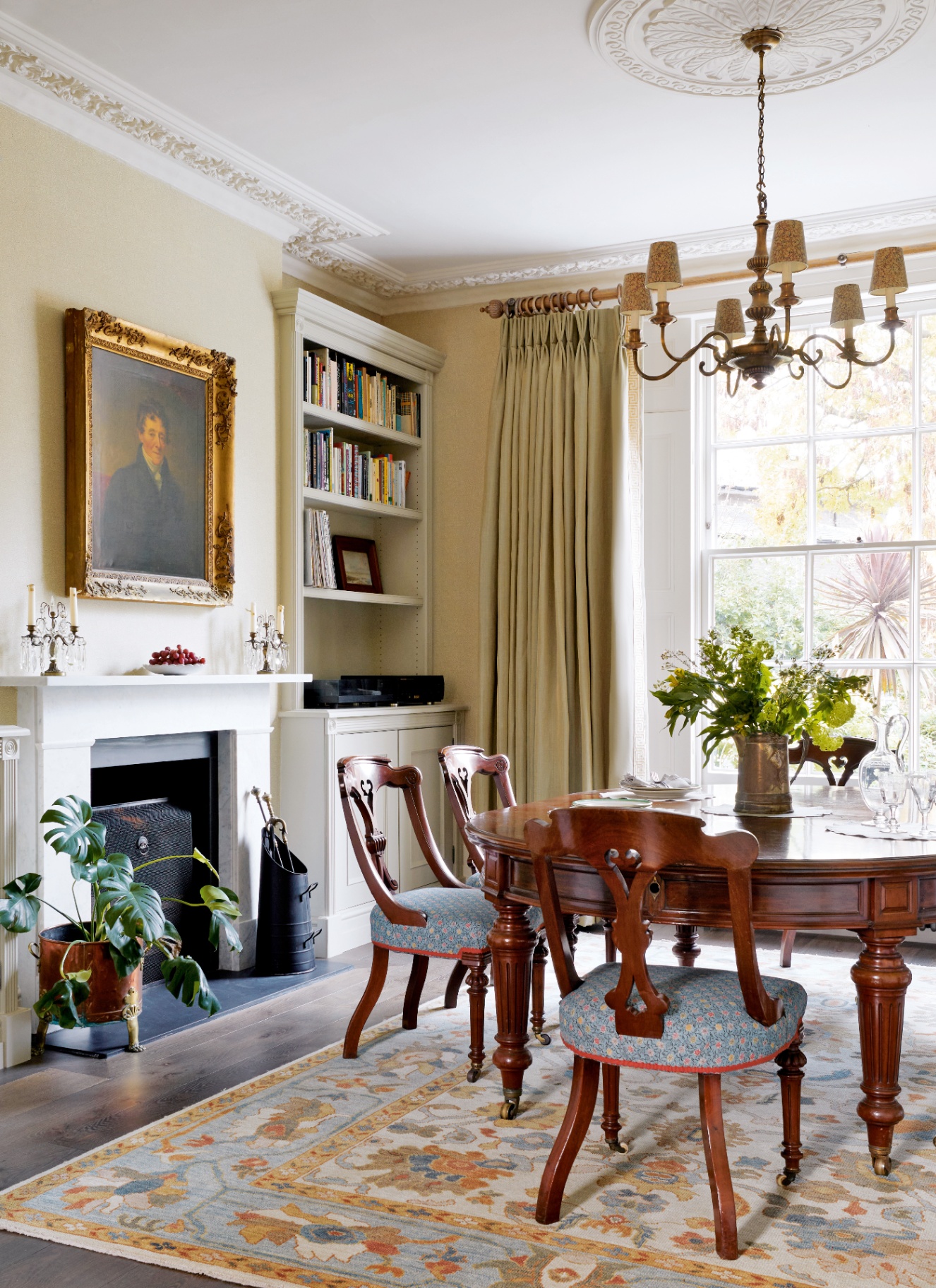 Elegant neutral dining room featuring textured light cream walls, a white marble fireplace, mahogany dining table, traditional brass chandelier, and a large sash window