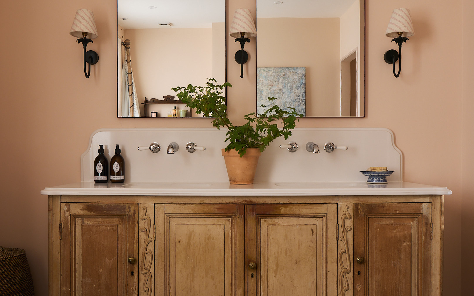 a statement antique style double vanity bathroom dresser pictured in wood with two mirrors on the wall above it and wall lamps