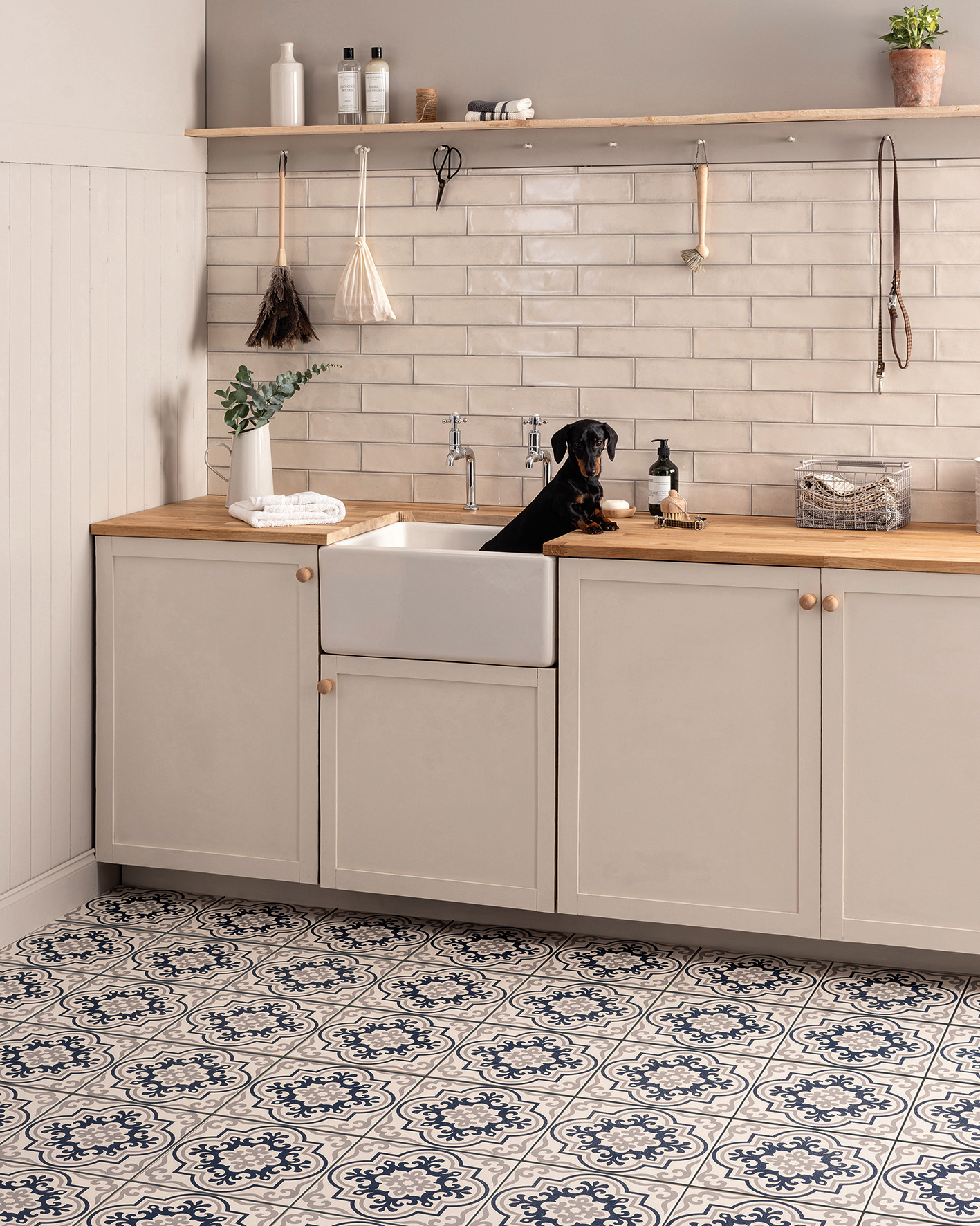 a utility room with neutral cabinets, a sausage dog in the sink and patterned tile floor