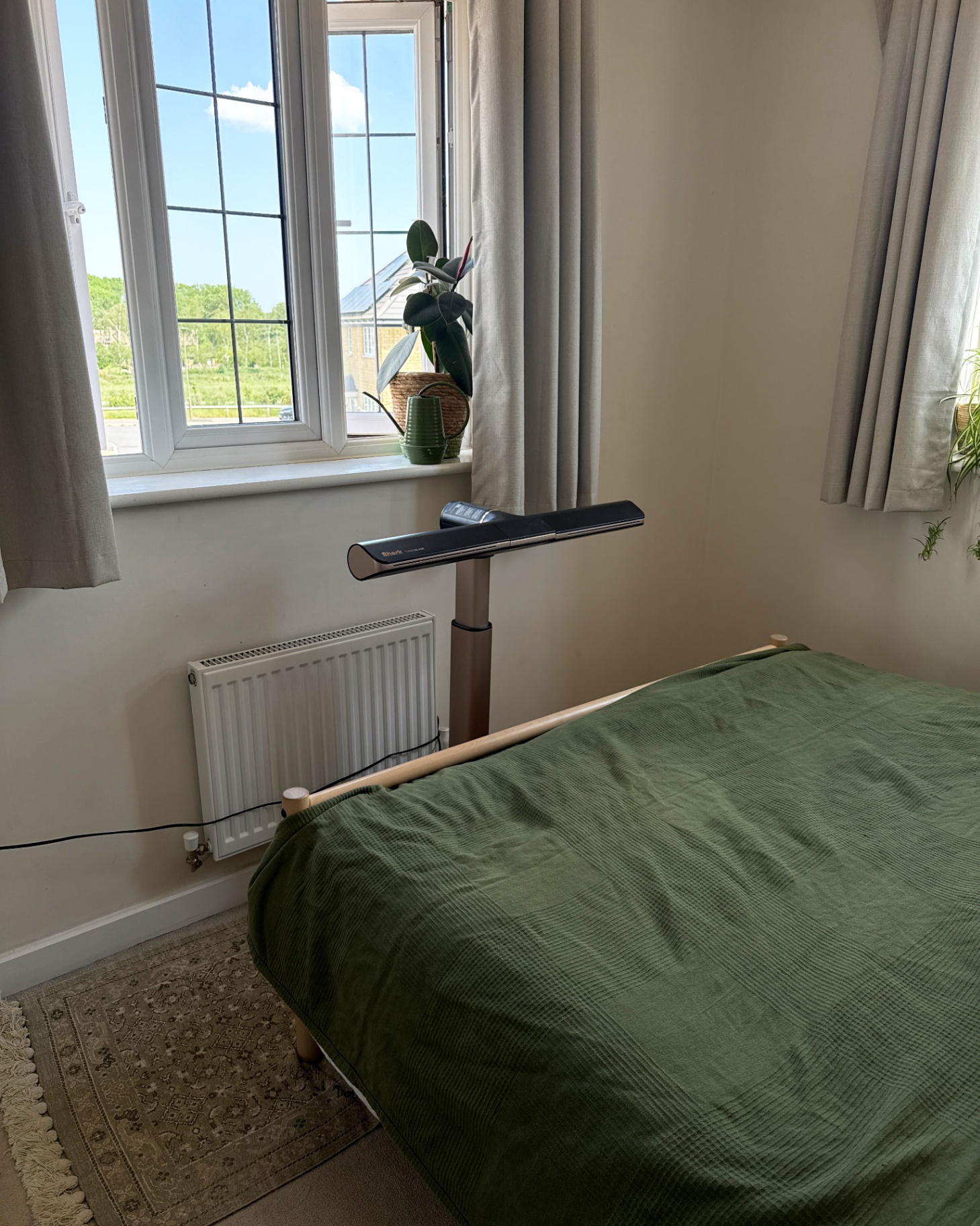 shark turboblade fan at the foot of a bed with a green bedspread in front of a window with grey curtains