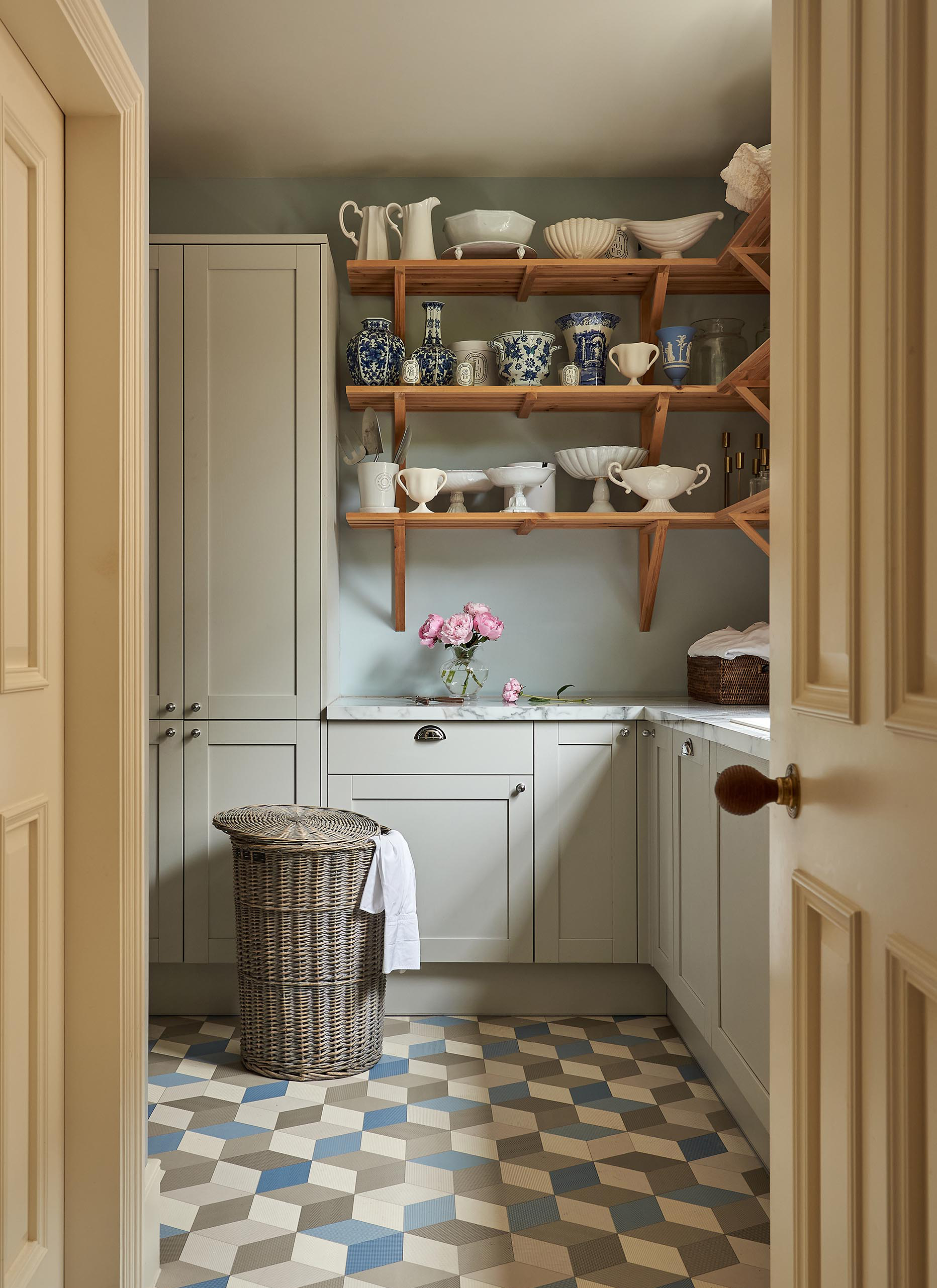 a utility room with pale grey cabinetry, grey and blue geometric flooring and wooden open shelves with china