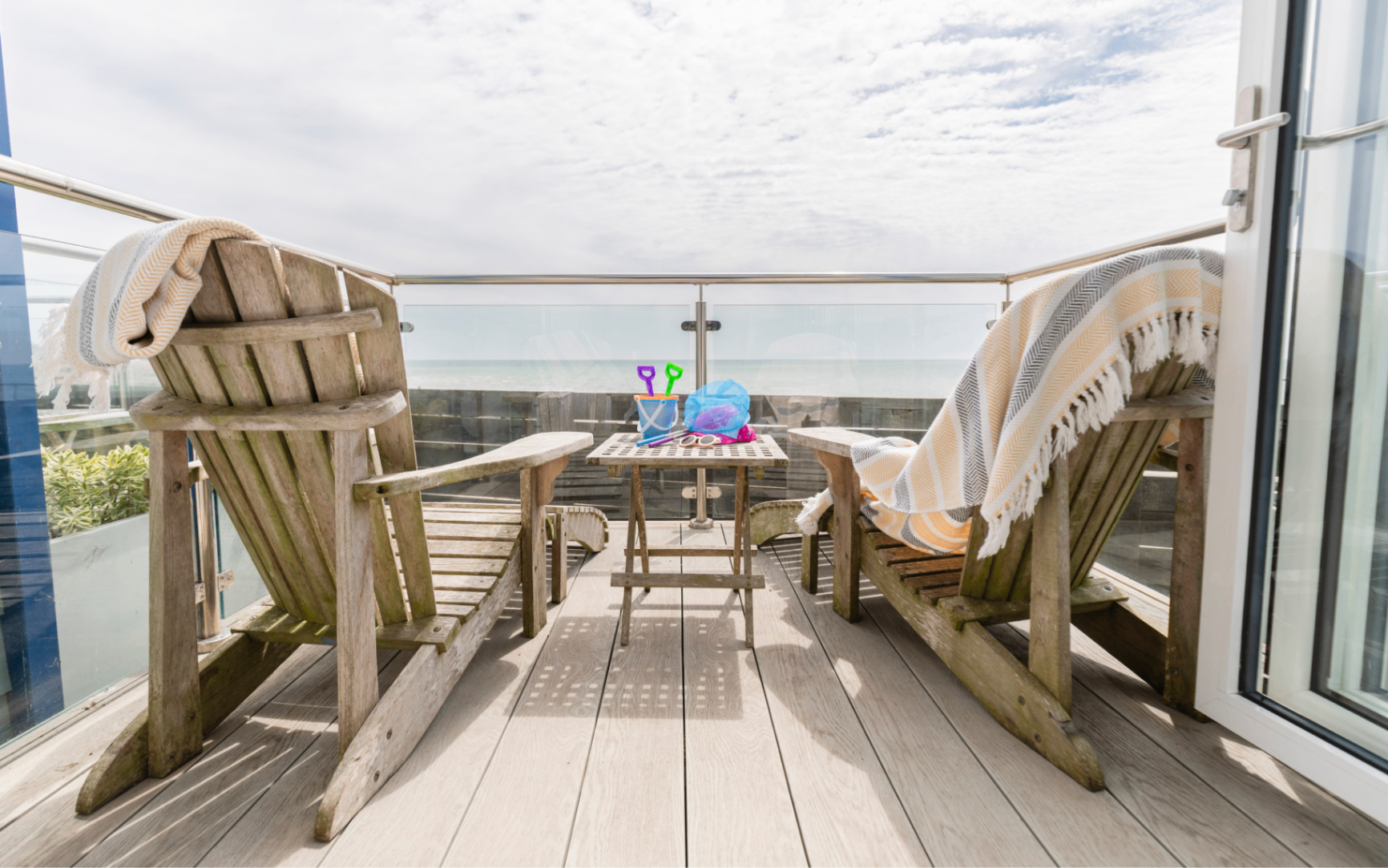 a beach hut balcony with two wooden lounge chairs and a coffee table facing the view of the sea
