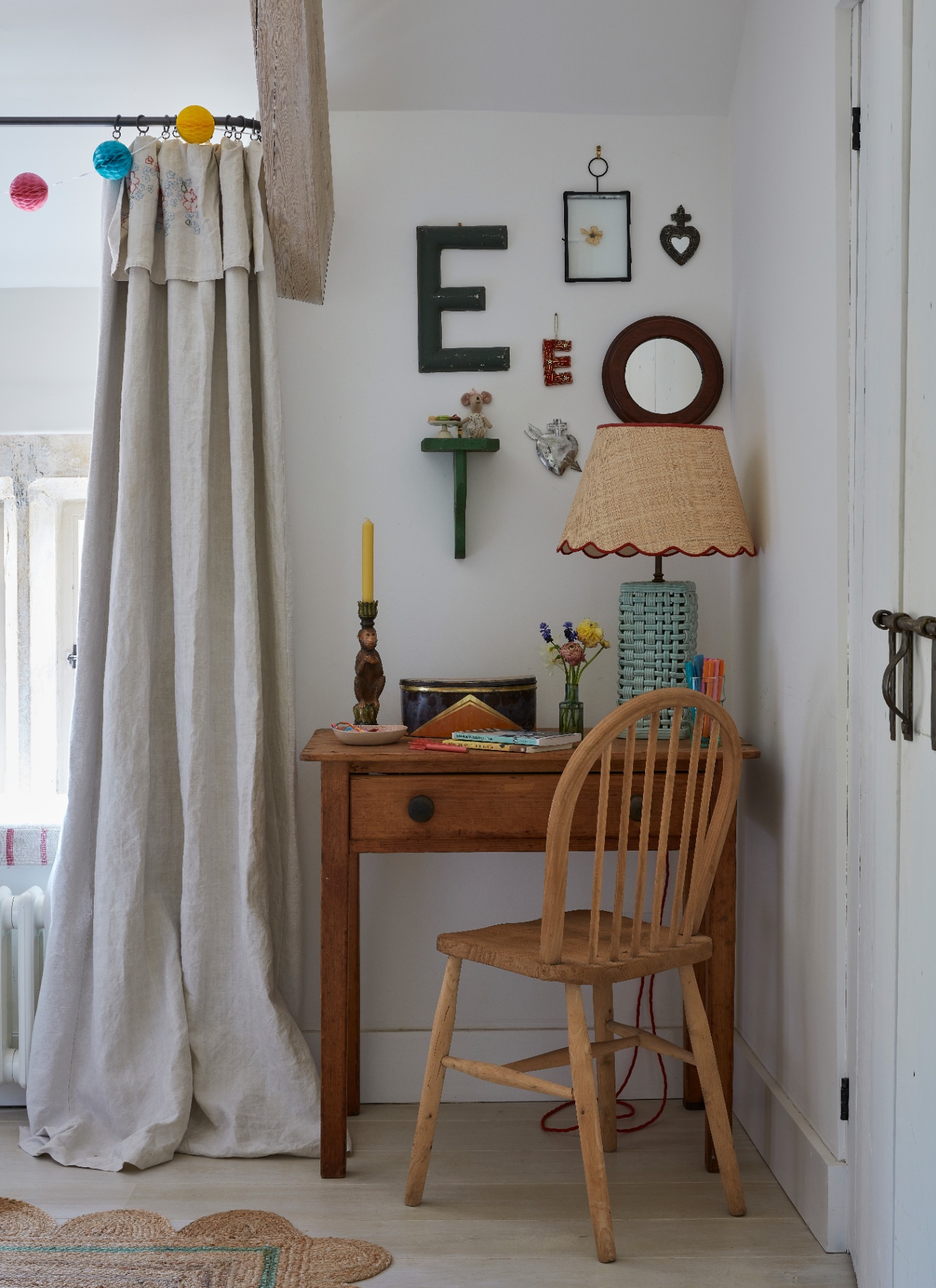 a close up of a childrens bedroom corner with white walls, a wooden desk and chair and the letter E and other objects hung on the wall