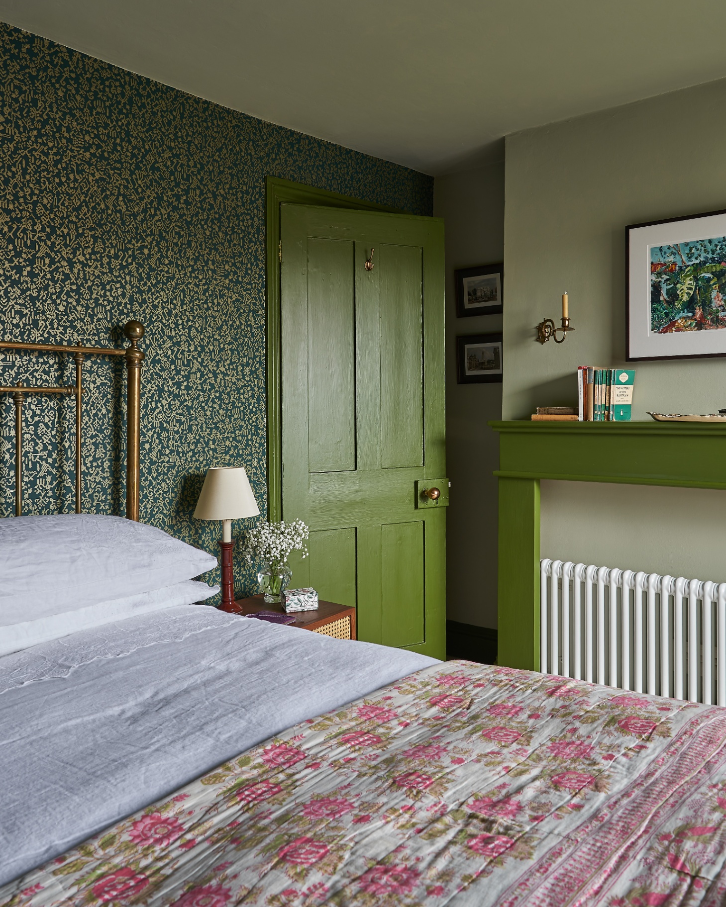 a bedroom with green floral wallpaper, bright green painted door and fireplace and a bed with a pink floral bedspread