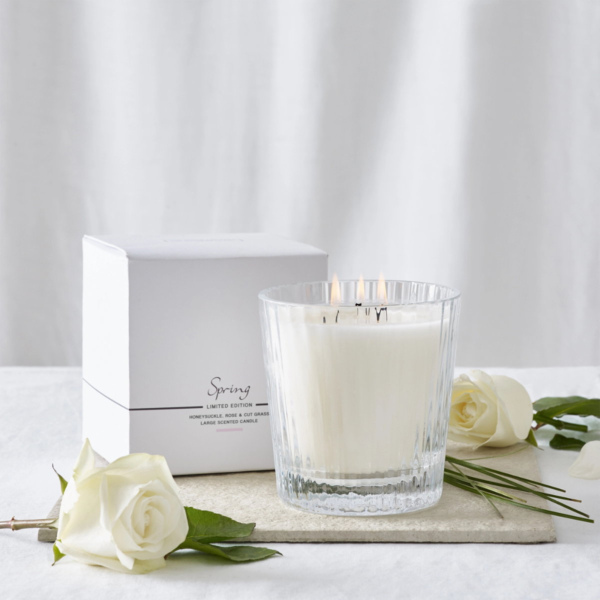 the white company spring candle in a clear glass ribbed vessel in front of the box