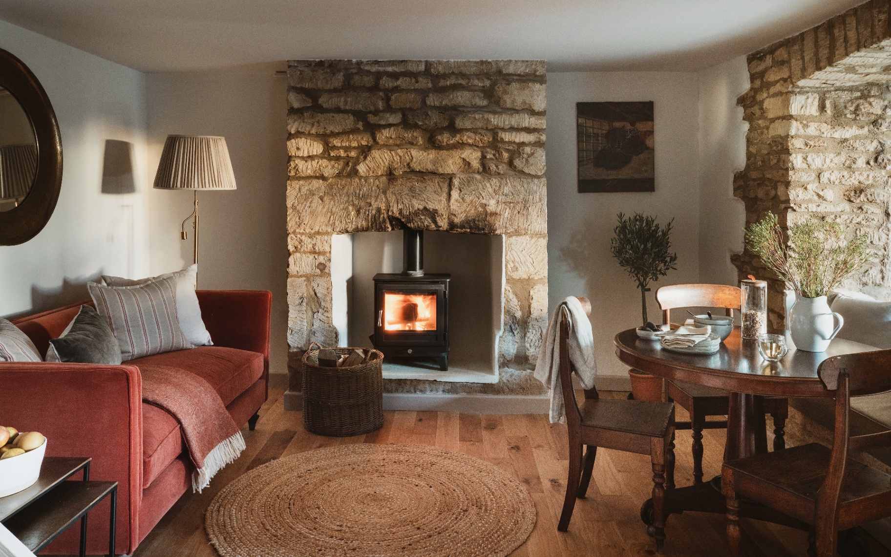 a living and dining area with a red velvet sofa, a wooden dining table and a large brick fireplace with a black wood burner