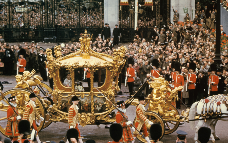 Queen Elizabeth II waving to the crowds after the coronation ceremony, travelling in the Gold State Coach
