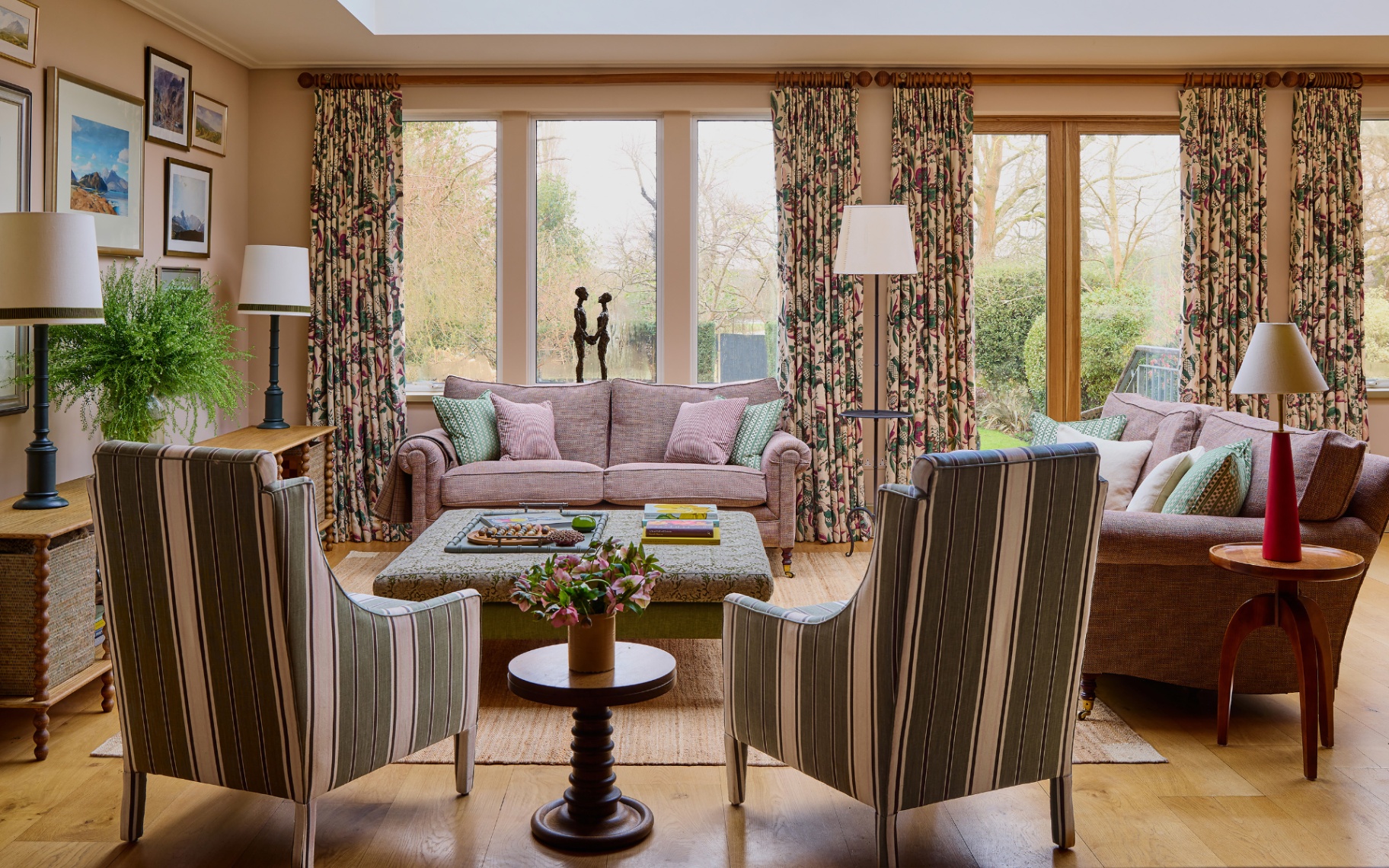 a living room with two striped armchairs in the foreground, a red and white stripe sofa at the back and at the right, two sets of floral curtains on the back wall over the windows and an ottoman coffee table in the middle