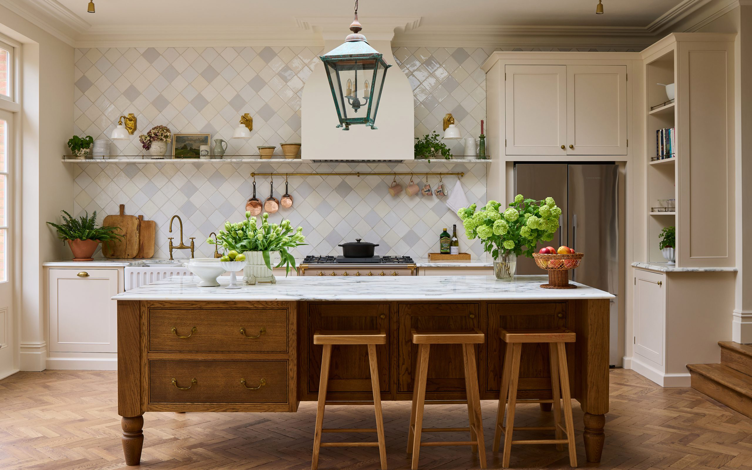 a neutral kitchen with white tiled walls, a large wooden kitchen island with 3 stools and a large pendant above it