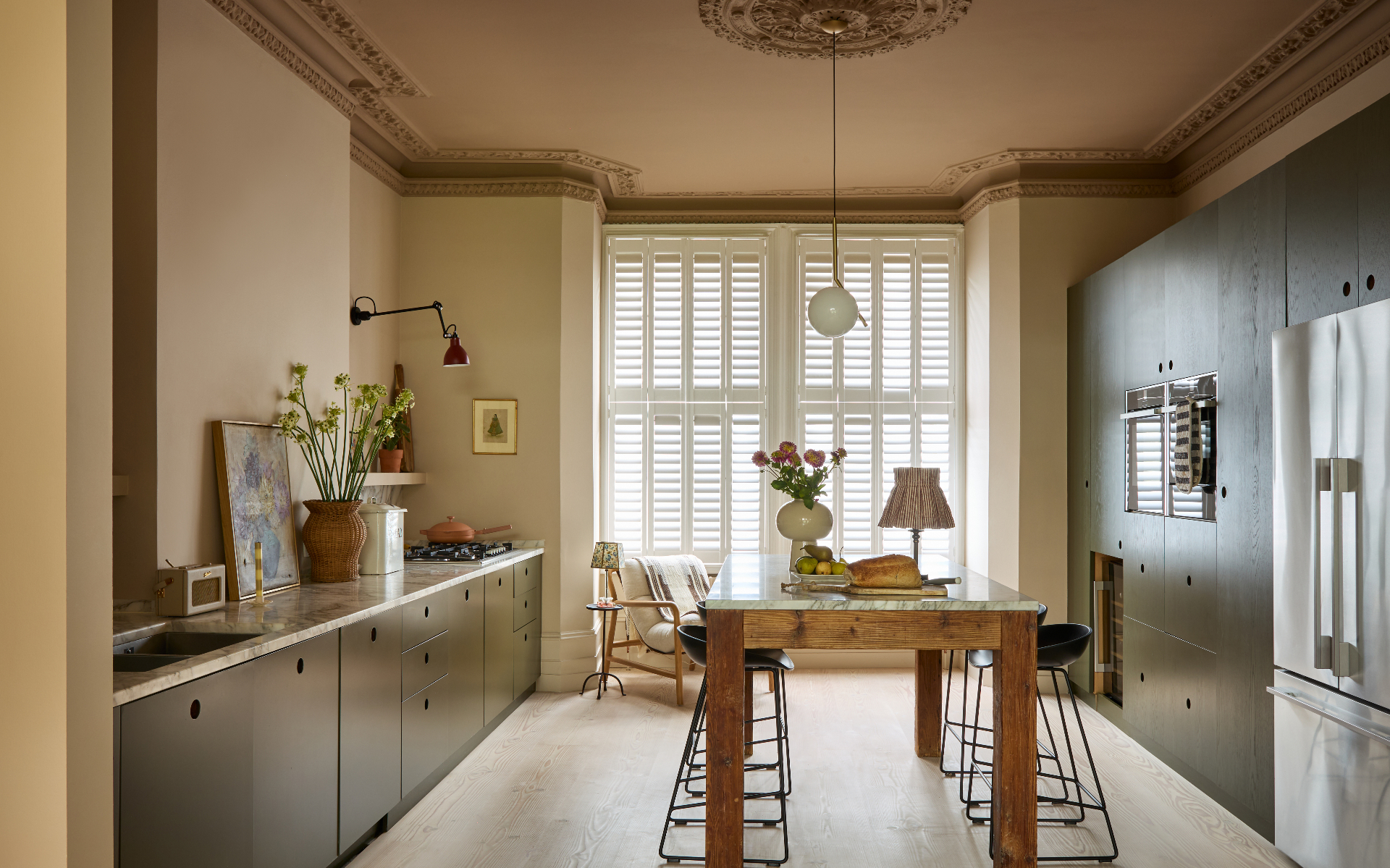 a kitchen with beige walls, a pale brown painted ceiling with ornate cornicing and a wooden dining table with black metal seats