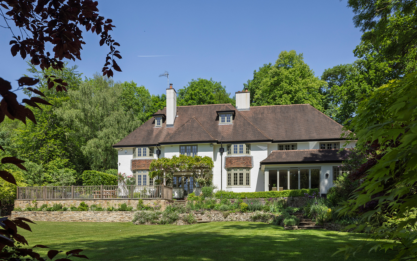 a three-storey country home covered in climbing plants set slightly elevated from a large garden lawn and surrounded by trees