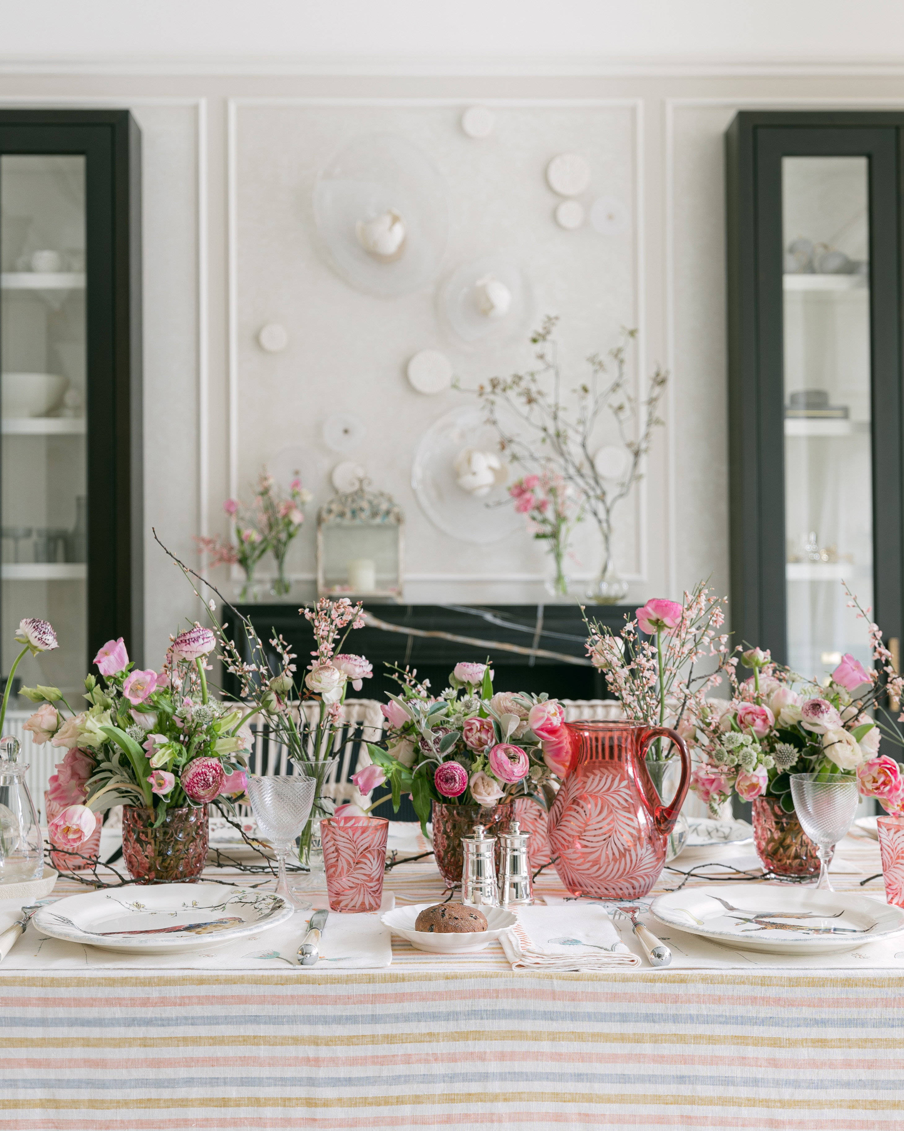 SPRING TABLESCAPE WITH A STRIPED TABLECLOTH AND VASES FILLED WITH PINK SPRING FLOWERS