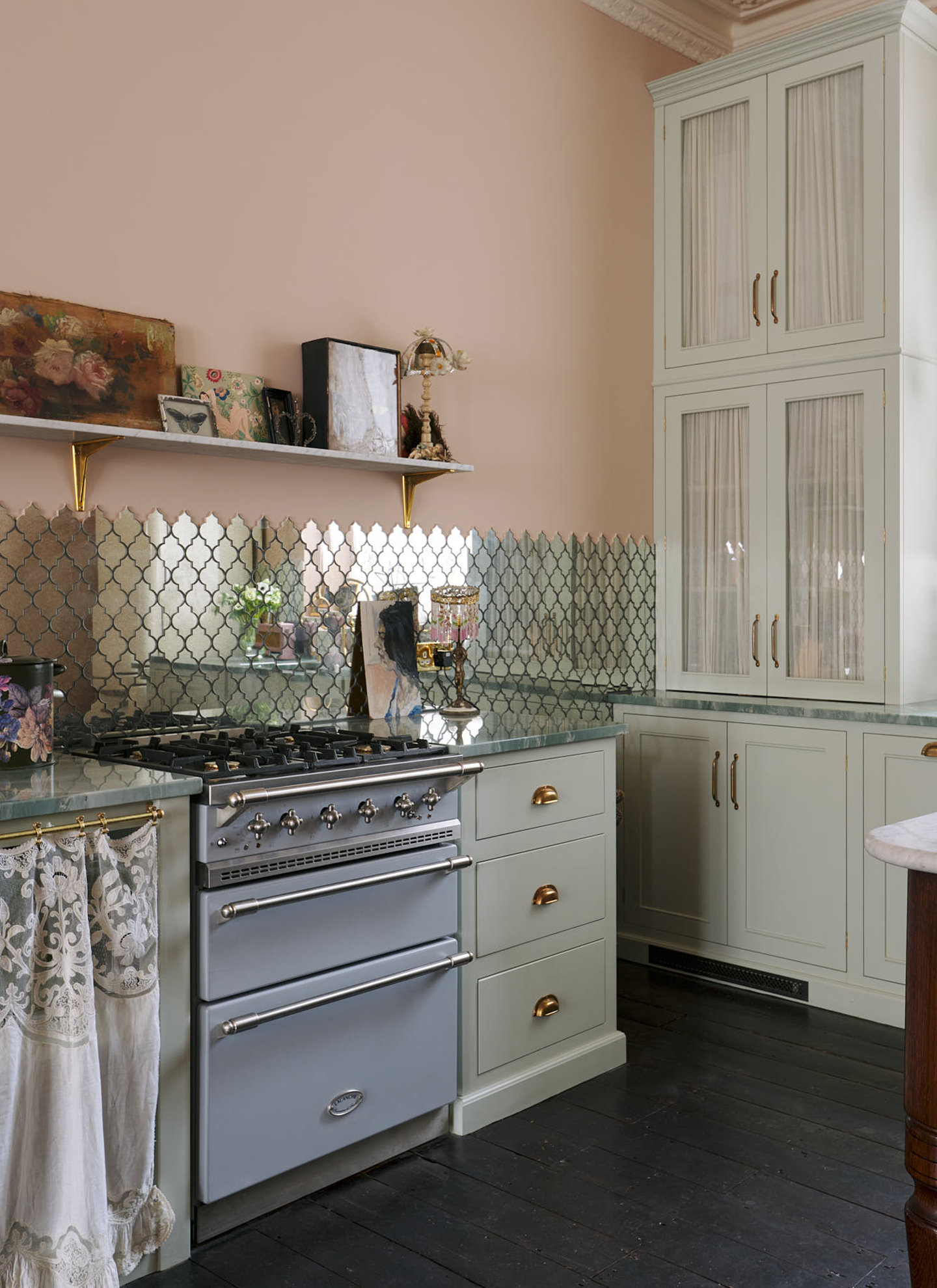 a kitchen with pale pink walls, a large white glass fronted cabinet, a pale blue range cooker and mirrored tile splashback