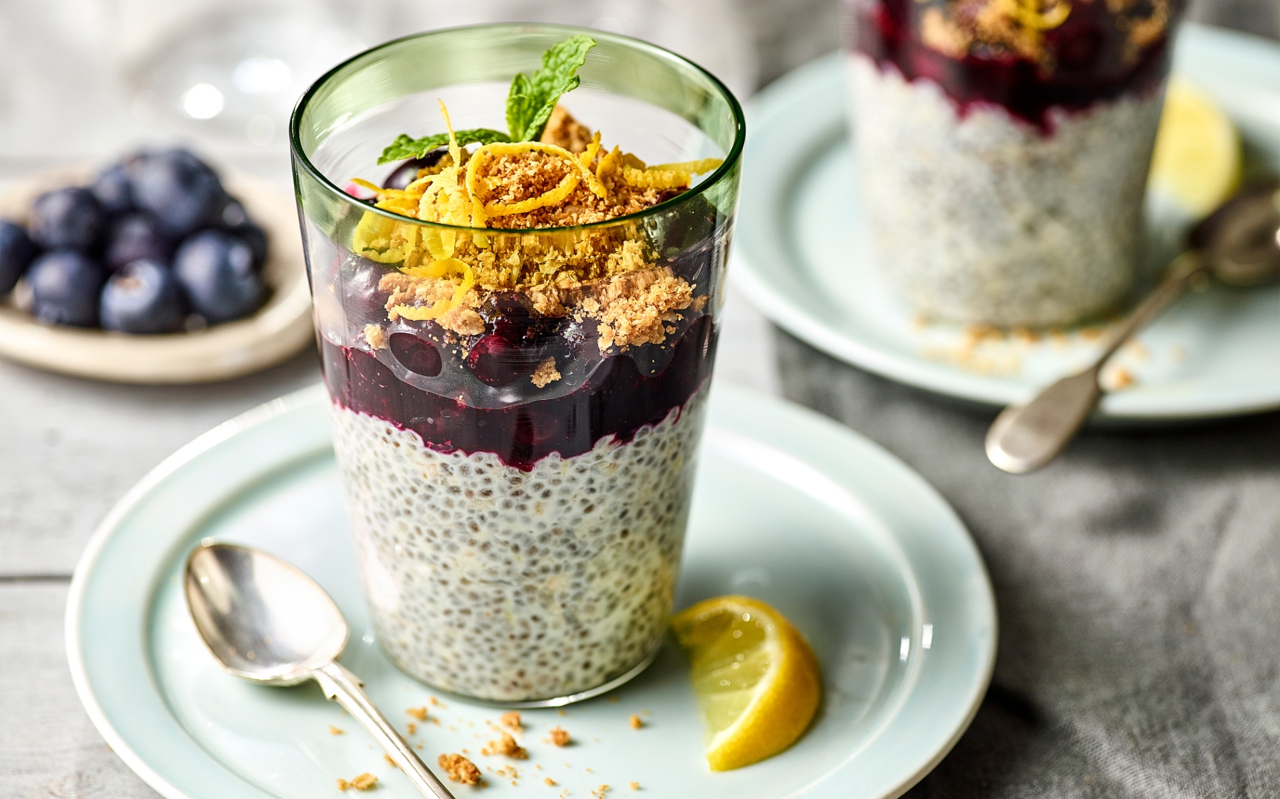 lemon Blueberry Chia Pots in a glass tumbler on a pale blue plate