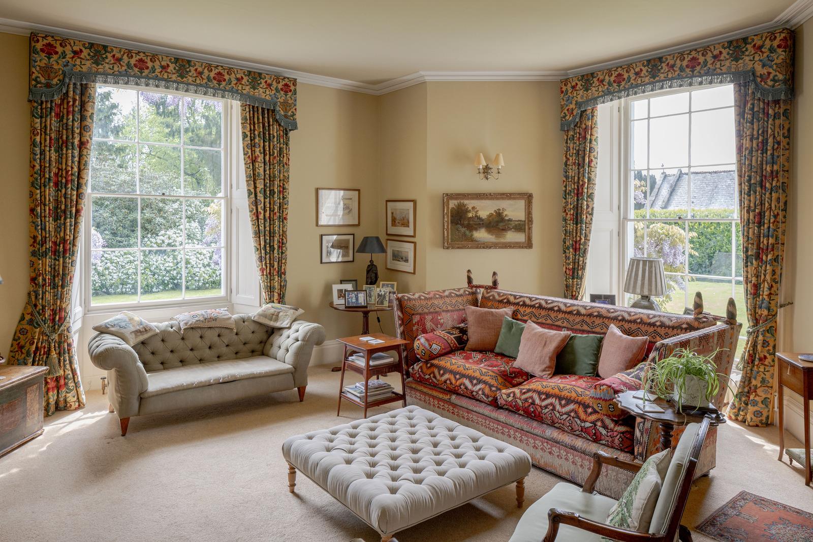 a living room with cream walls, yellow and blue floral curtains, a multicoloured ikat sofa and a pale grey upholstered coffee table
