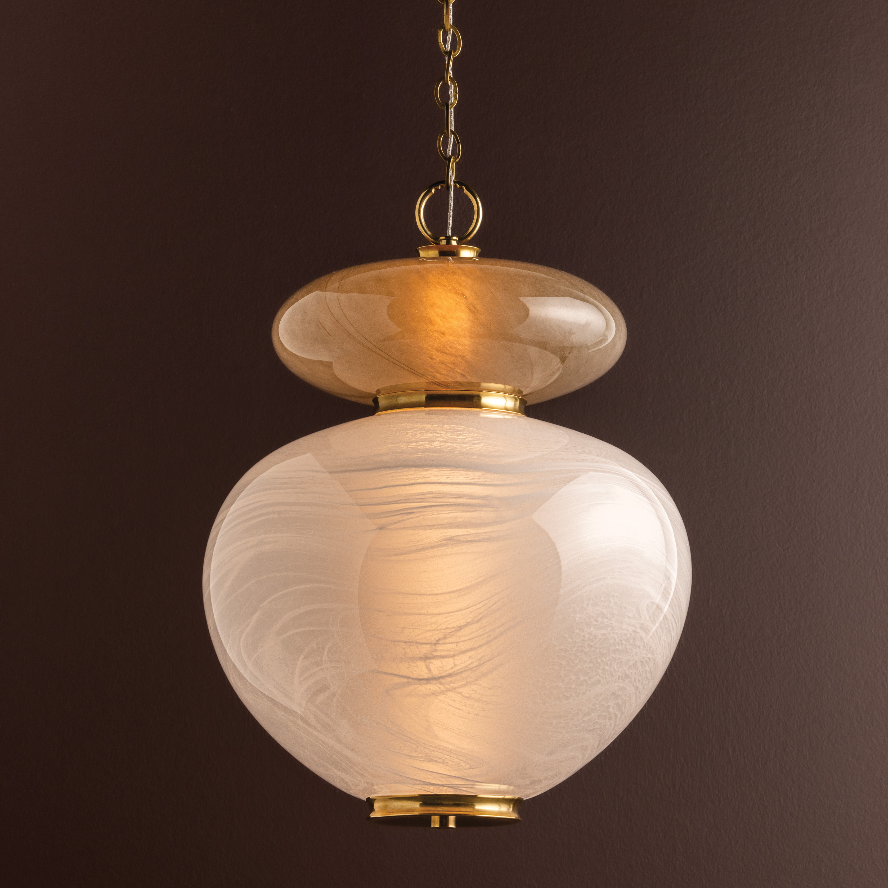 a two tone glass globe pendant light with gold hardware on a dark brown background