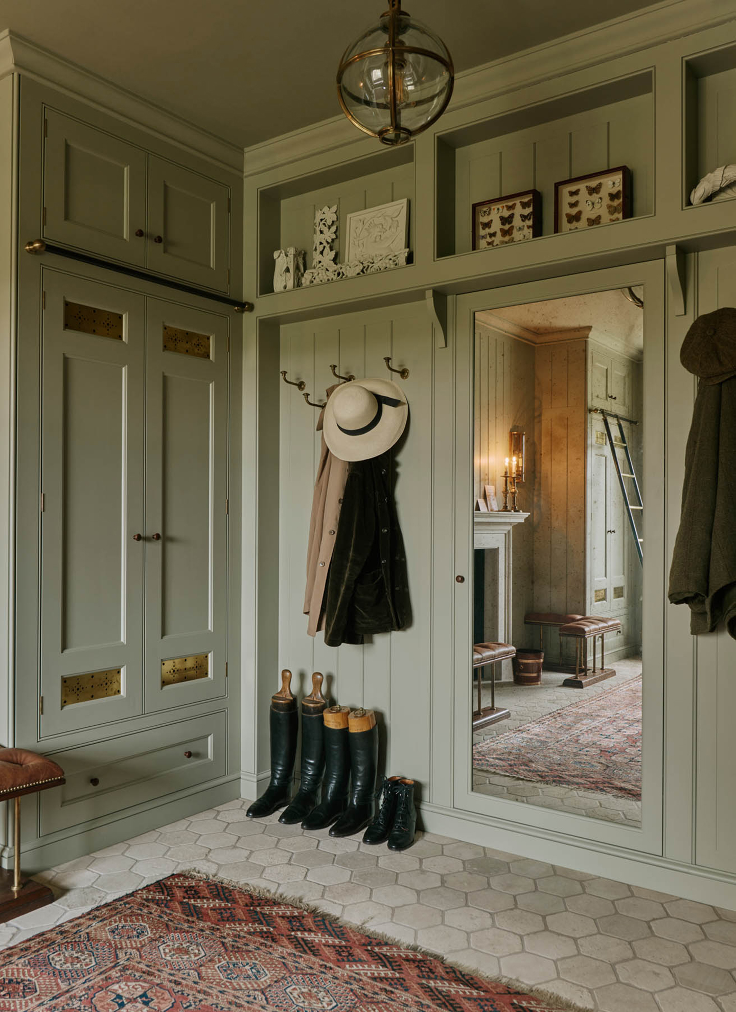 a boot room with sage green cabinets, hexagonal tiled flooring and a floor length mirror