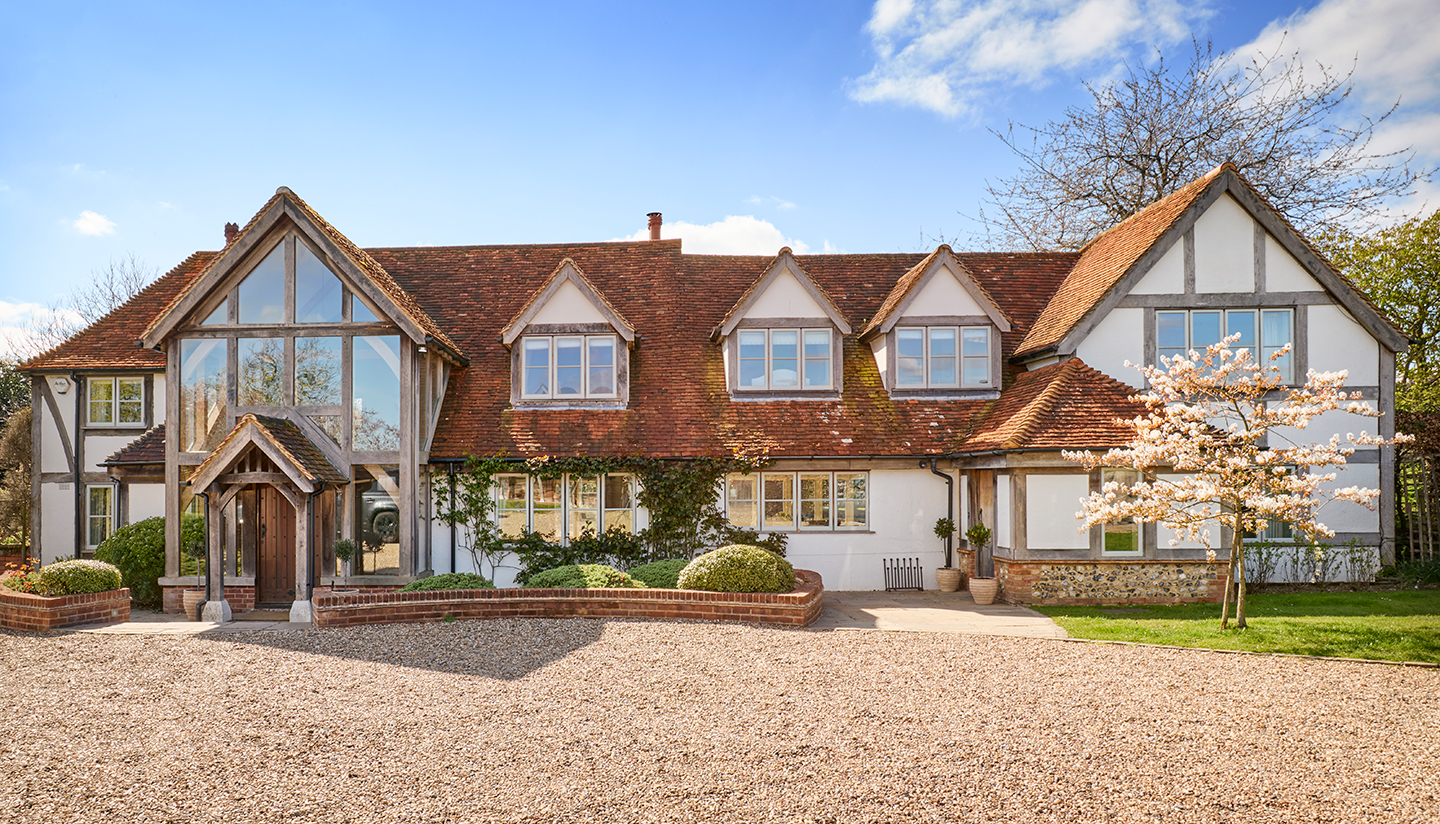 A large country house with tiled roof, beams and a large glazed extension on the front 