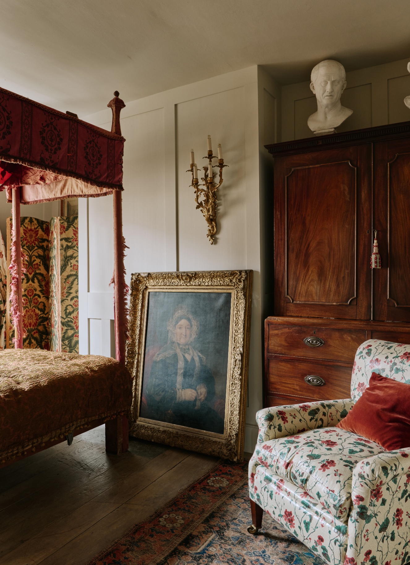 A traditional period bedroom featuring an ornate three-arm gilt candelabra wall sconce mounted on cream paneled walls next to a four-poster bed