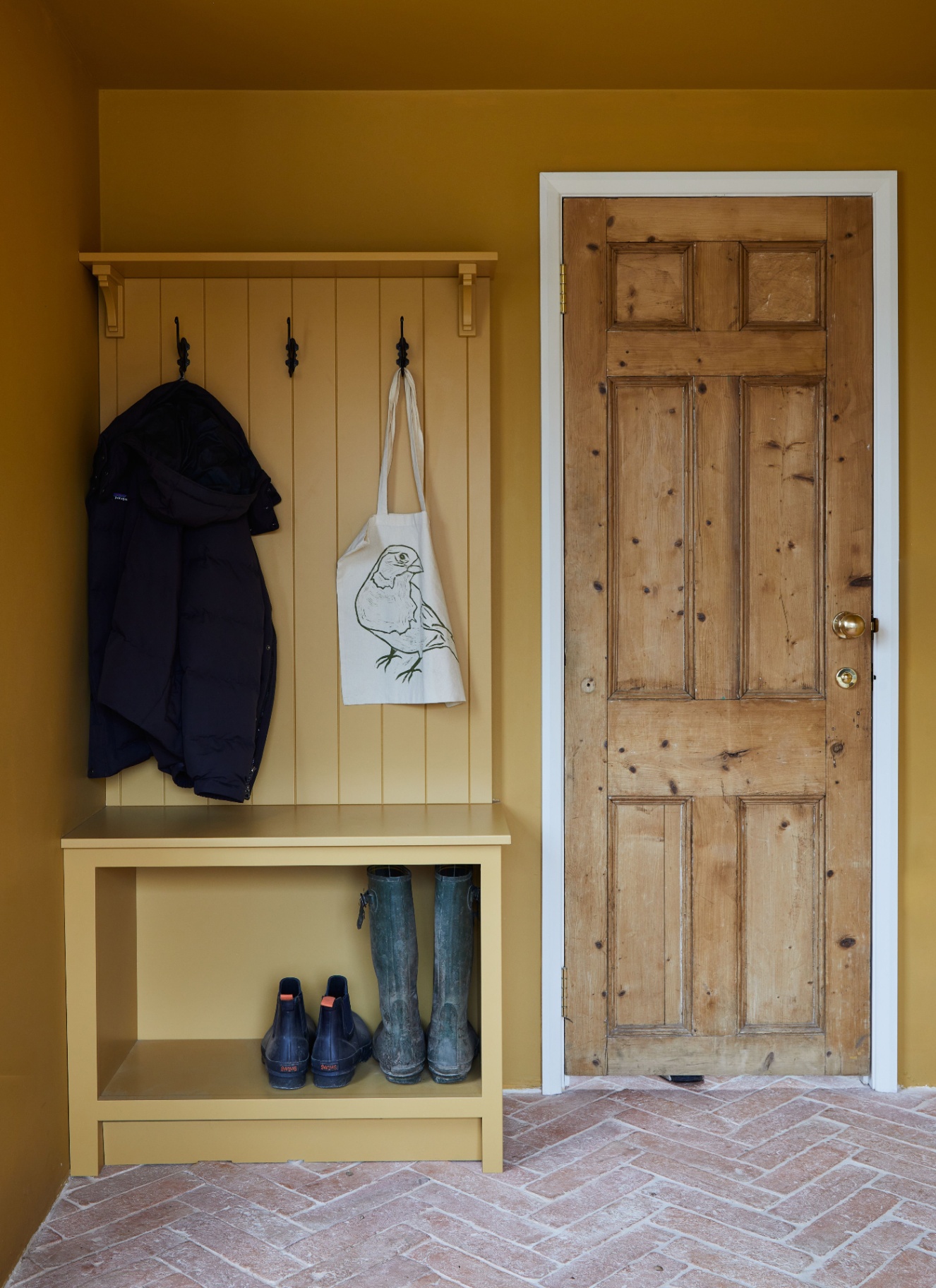 a small boot room area next to a wooden door with walls and joinery painted in mustard yellow