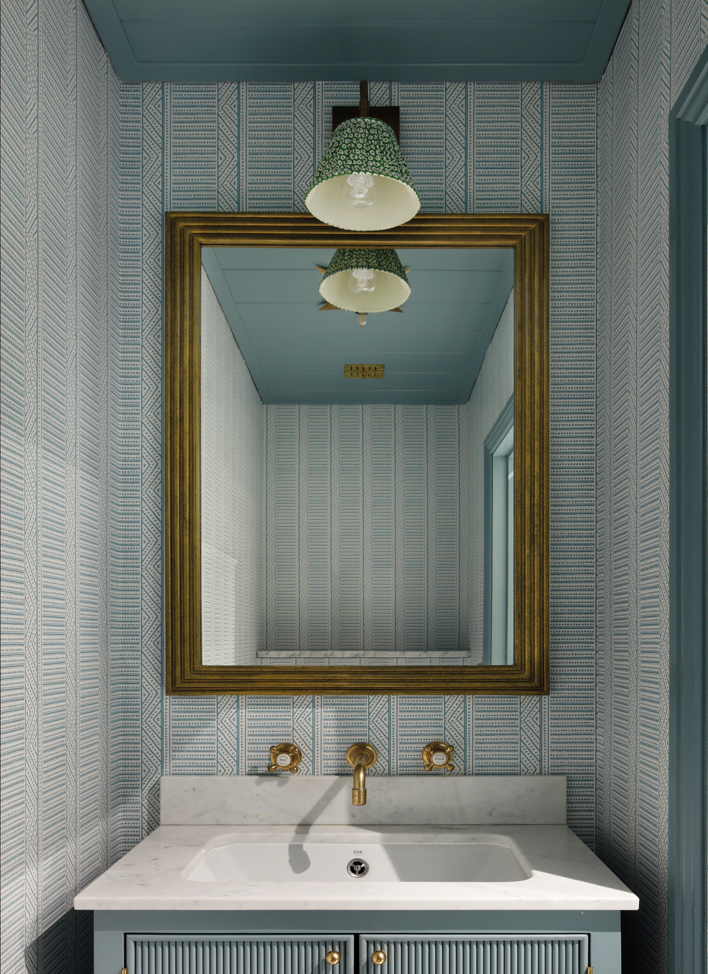 a small downstairs toilet with white and blue patterned wallpaper, a blue ceiling and a large gold mirror above the sink