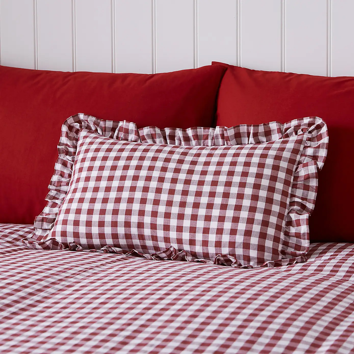 a red and white gingham ruffled cushion in front of red pillows and on top of a red gingham duvet set