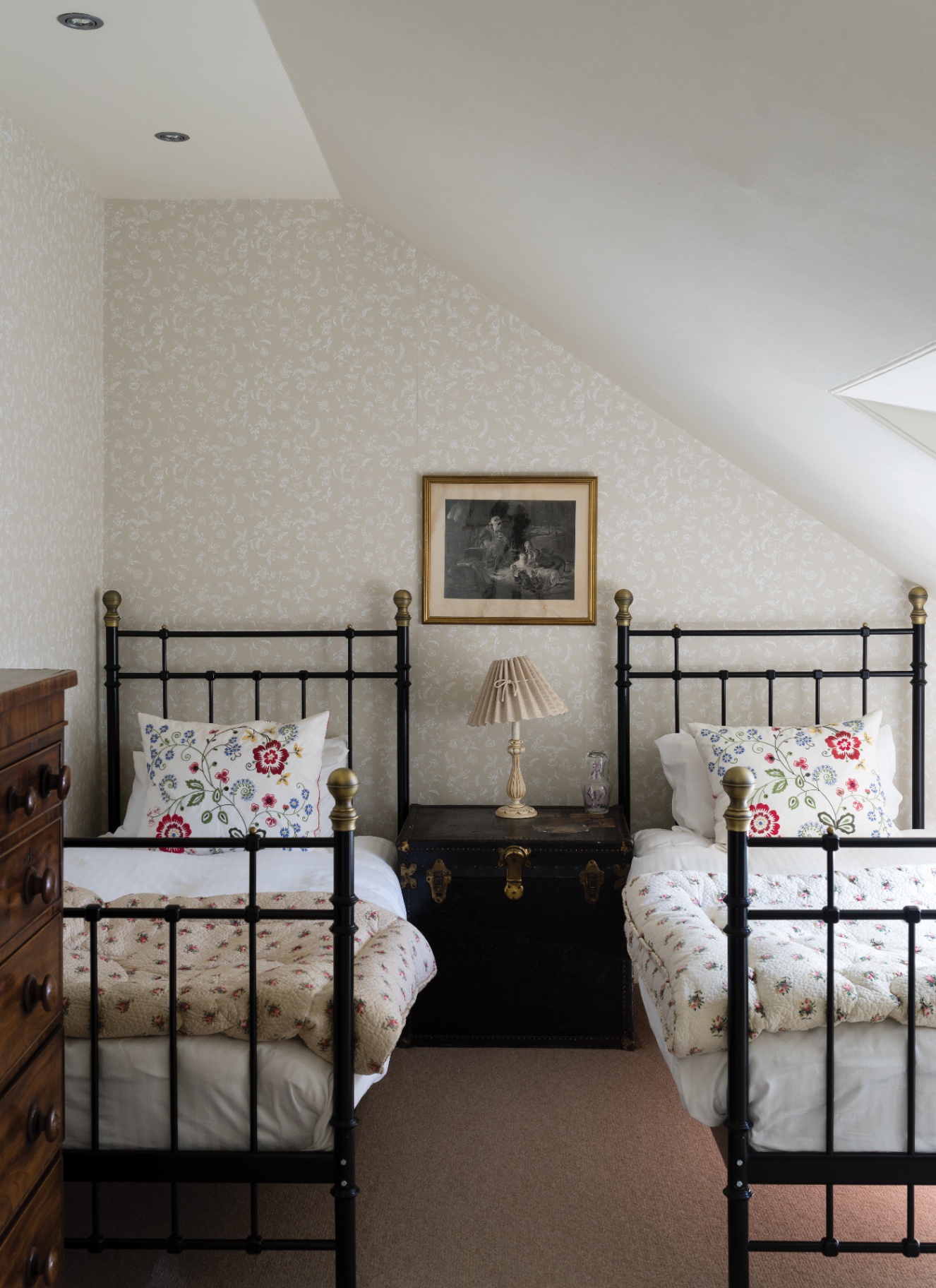a bedroom with sloping ceilings, beige and white patterned wallpaper and two twin black iron framed beds
