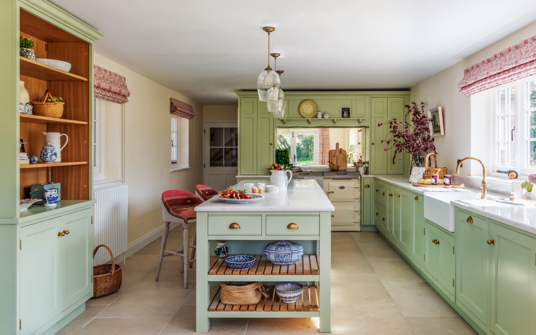 a kitchen with green painted cabinets, a sage green kitchen island with two red stools and 3 matching glass pendant shades above it
