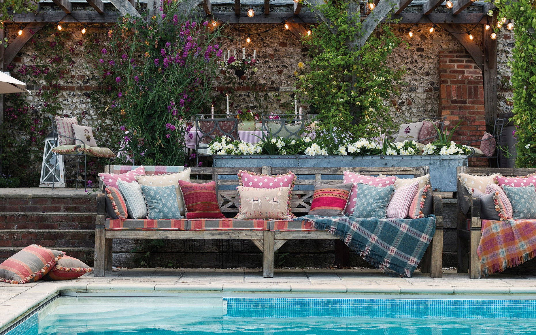 an outdoor dining set up pictured with a pool and outdoor cushions and blankets scattered on a sofa by Susie Watson Designs 
