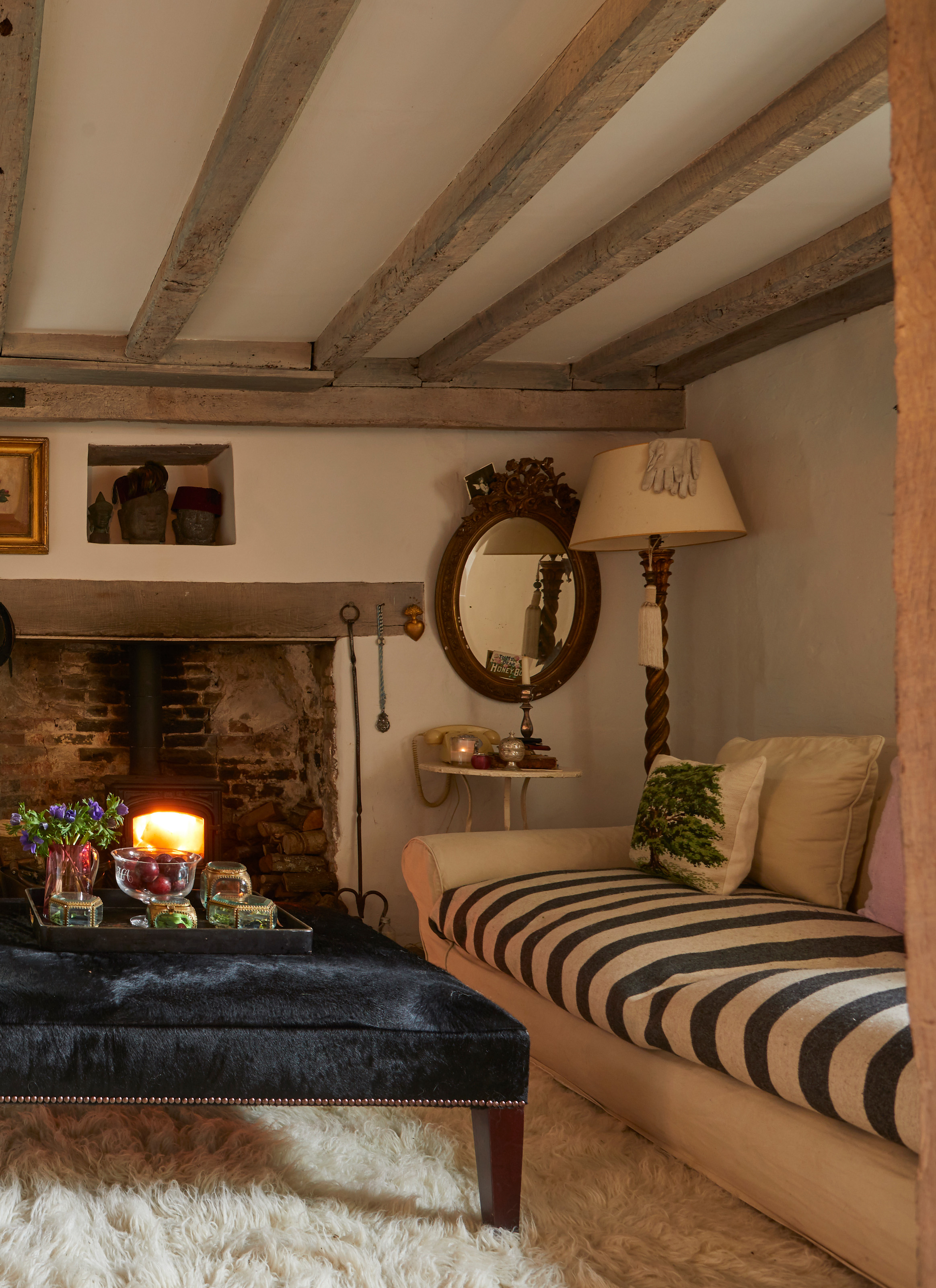 a cottage living room with a fireplace, a navy upholstered coffee table, a cream and stripe cofa and a wooden floor lamp