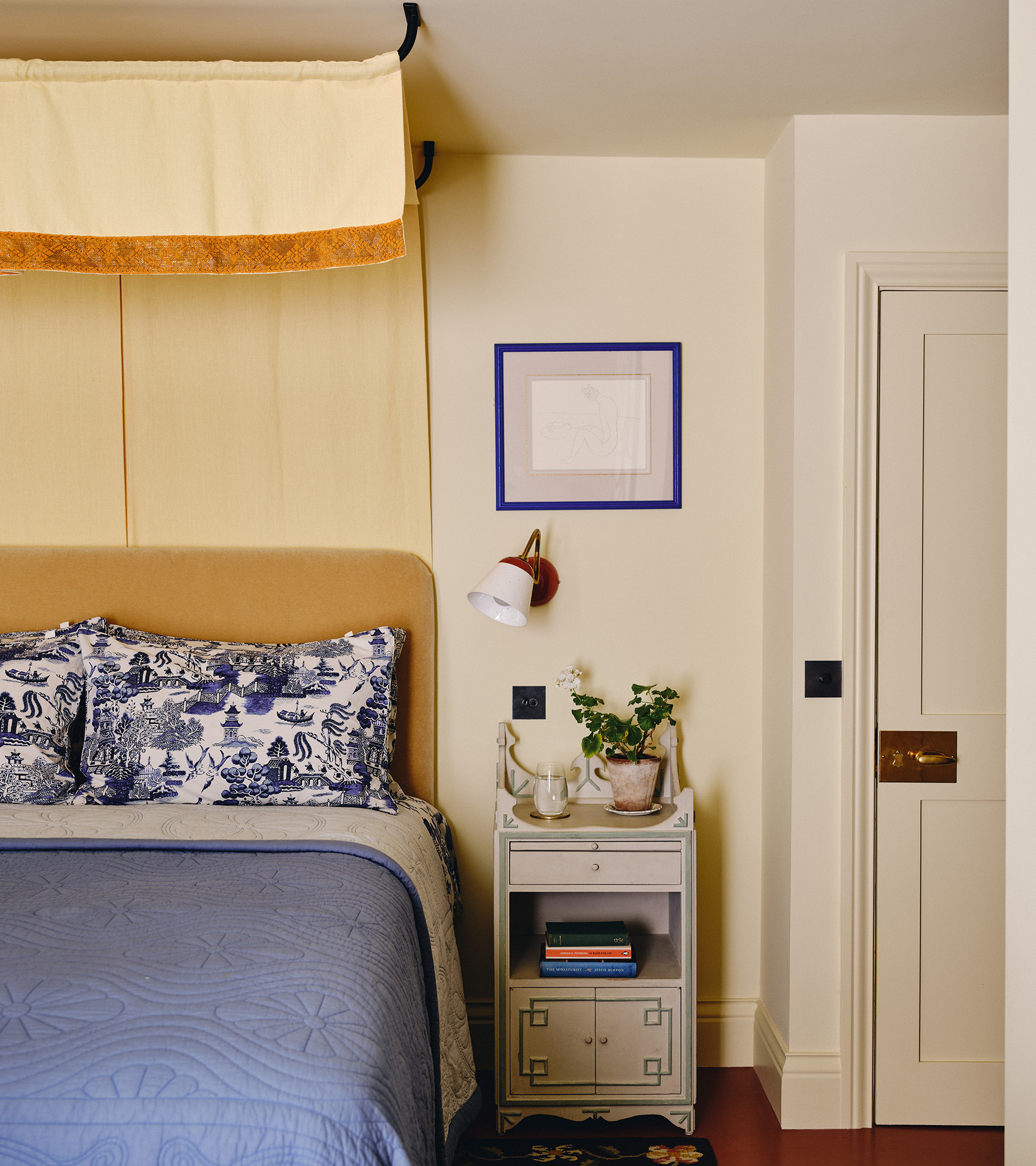 A bedroom with butter yellow canopy drapes above a bed with a yellow headboard and a blue bedspread