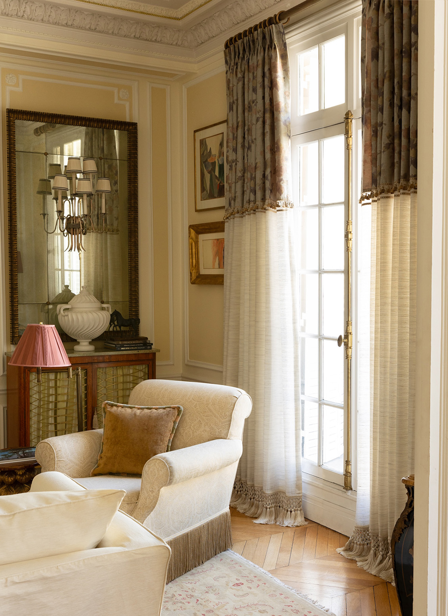 a living room with sheer curtains, a white fringed armchair and a large vintage mirror
