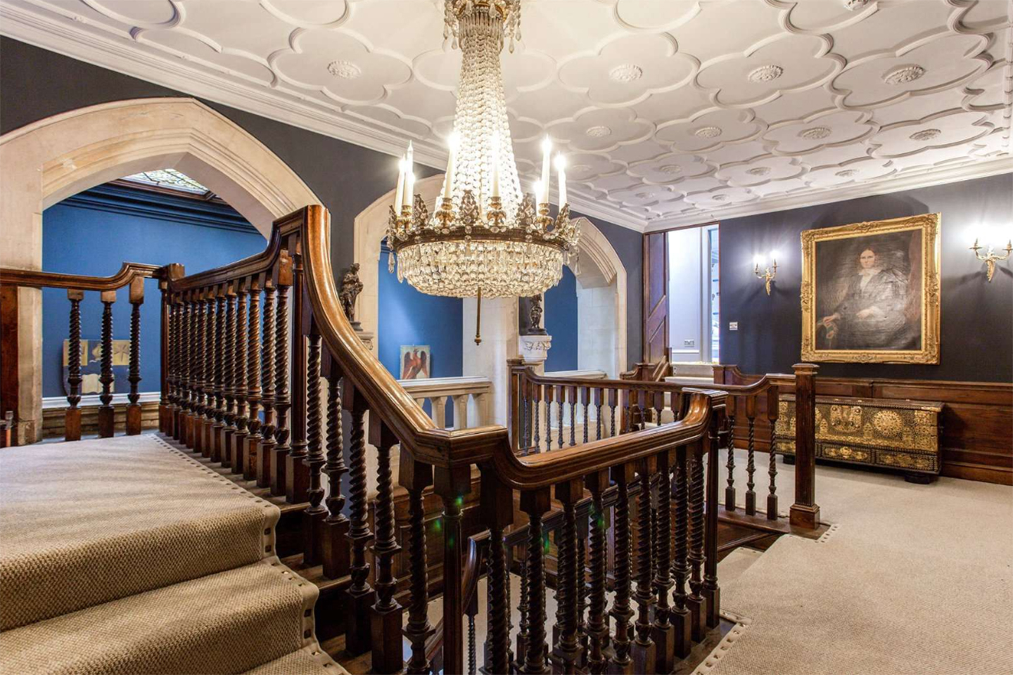 a grand upstairs hallway with navy walls, a large crystal chandellier and wooden banisters