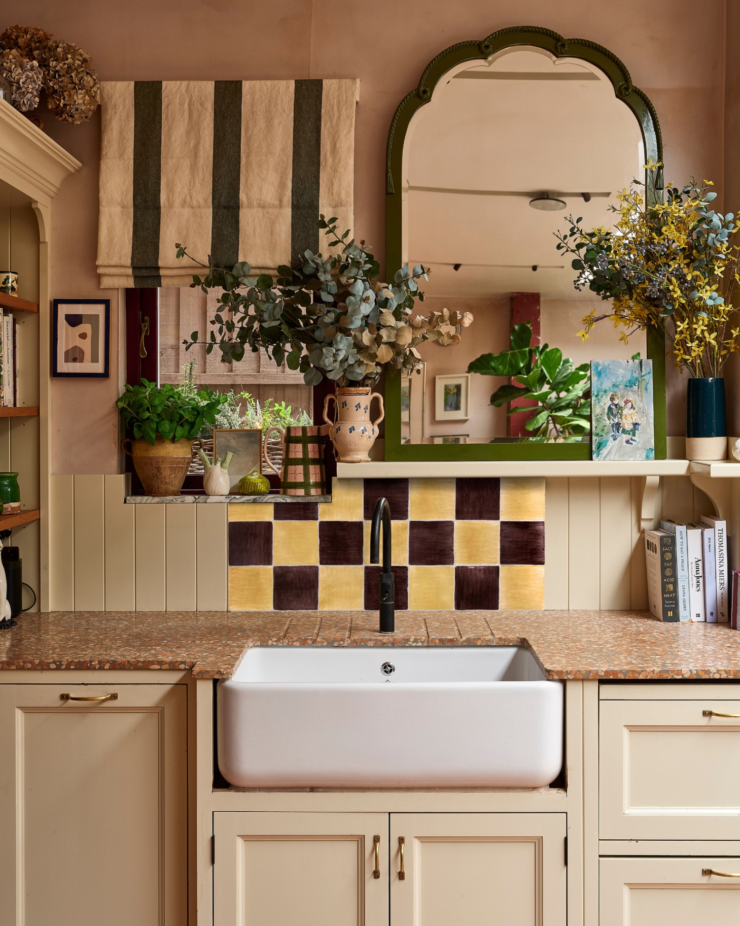 kitchen with yellow and brown checkerboard splashback behind a small belfast sink with an open shelf above with a large arched mirror
