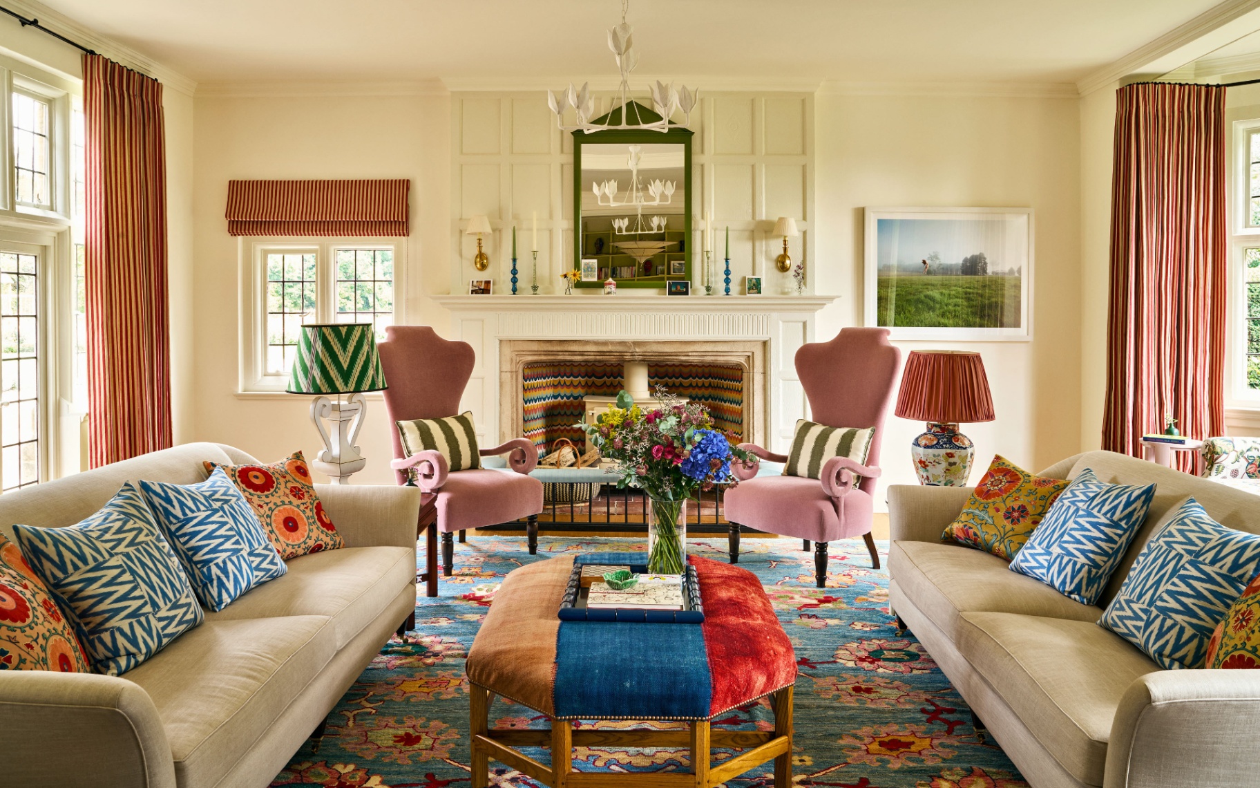 a living room with white walls, two cream sofas with patterned cushions and two pink velvet armchairs in front of a fireplace