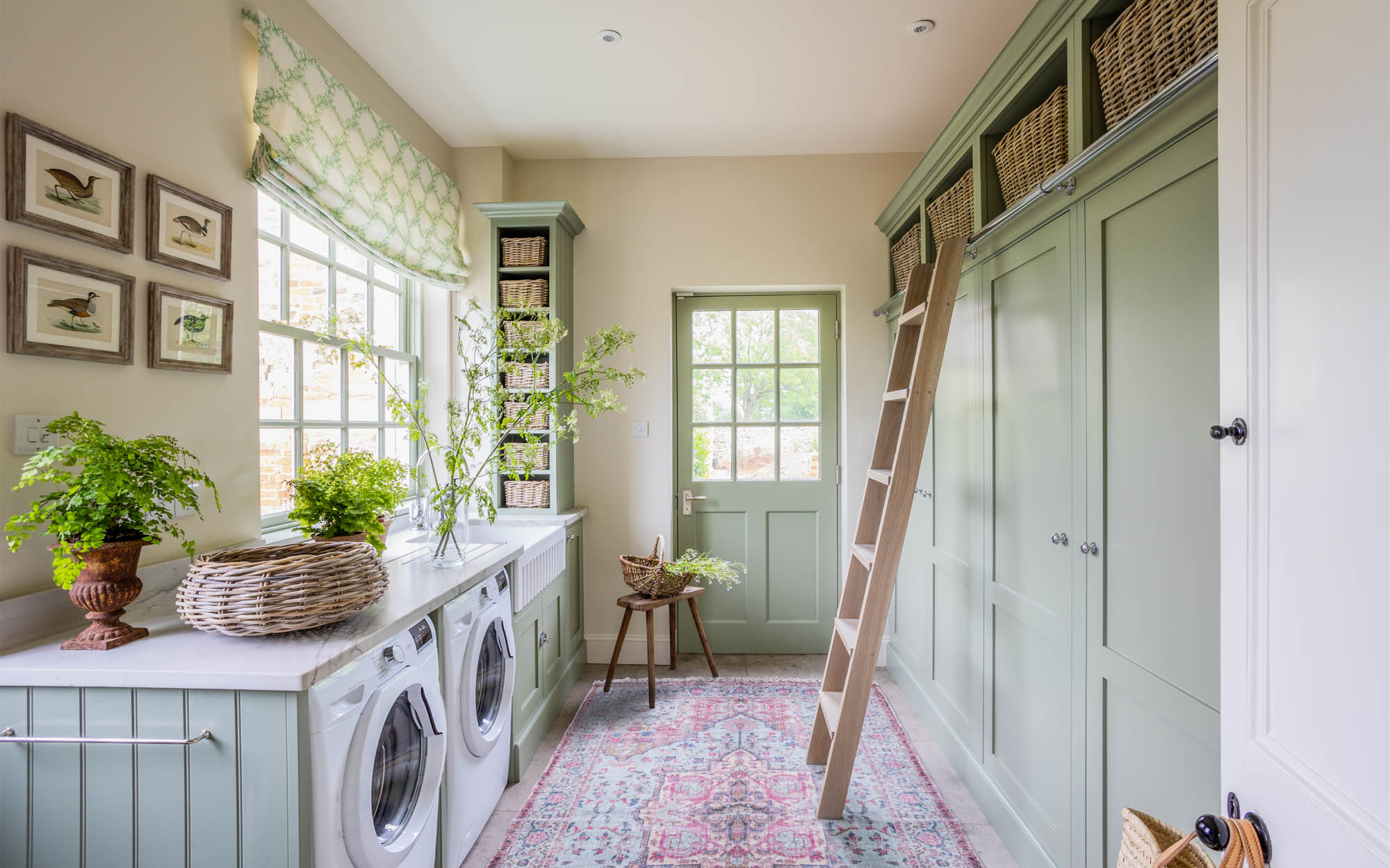 a utility room with sage green cabinets, a red persian rug, a library ladder leaning on the cabinets with wicker baskets above the cabinets
