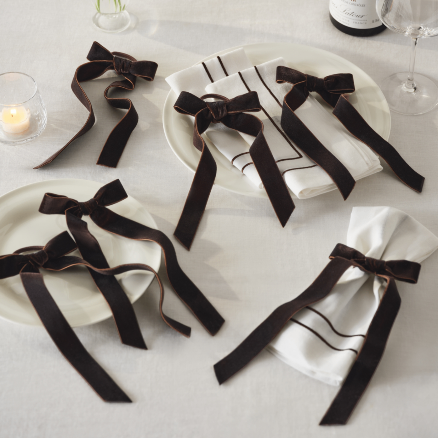 6 dark brown velvet bow napkin rings on a white table cloth with white napkins and two white plates