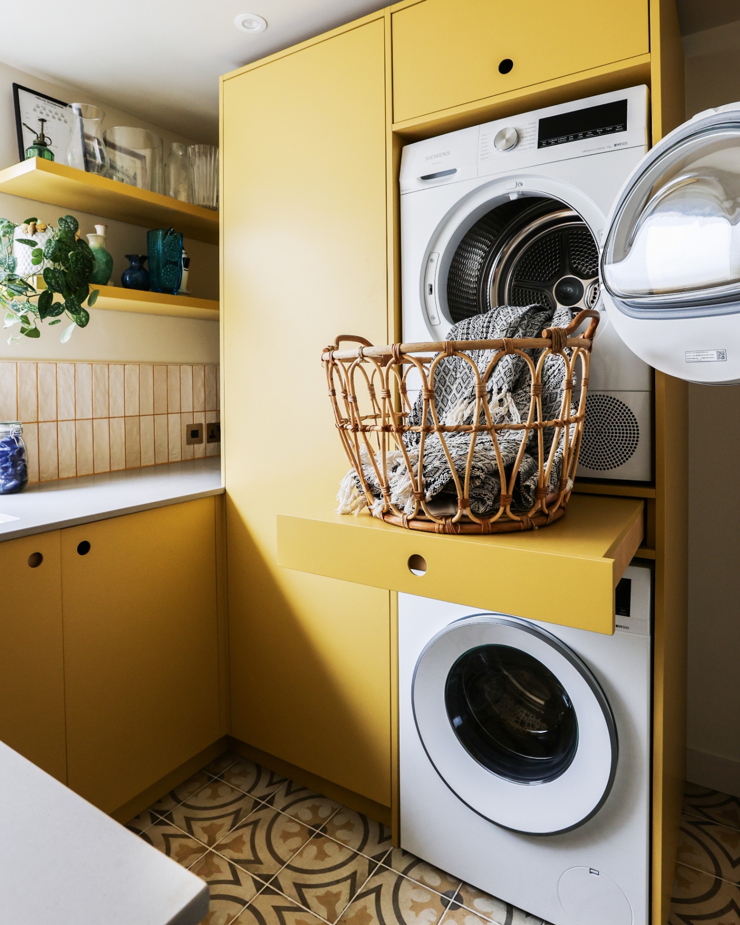 a utility room with bright yellow cabinets, a pull out folding station in the middle of two stacked washing machines with a wicker basket on top