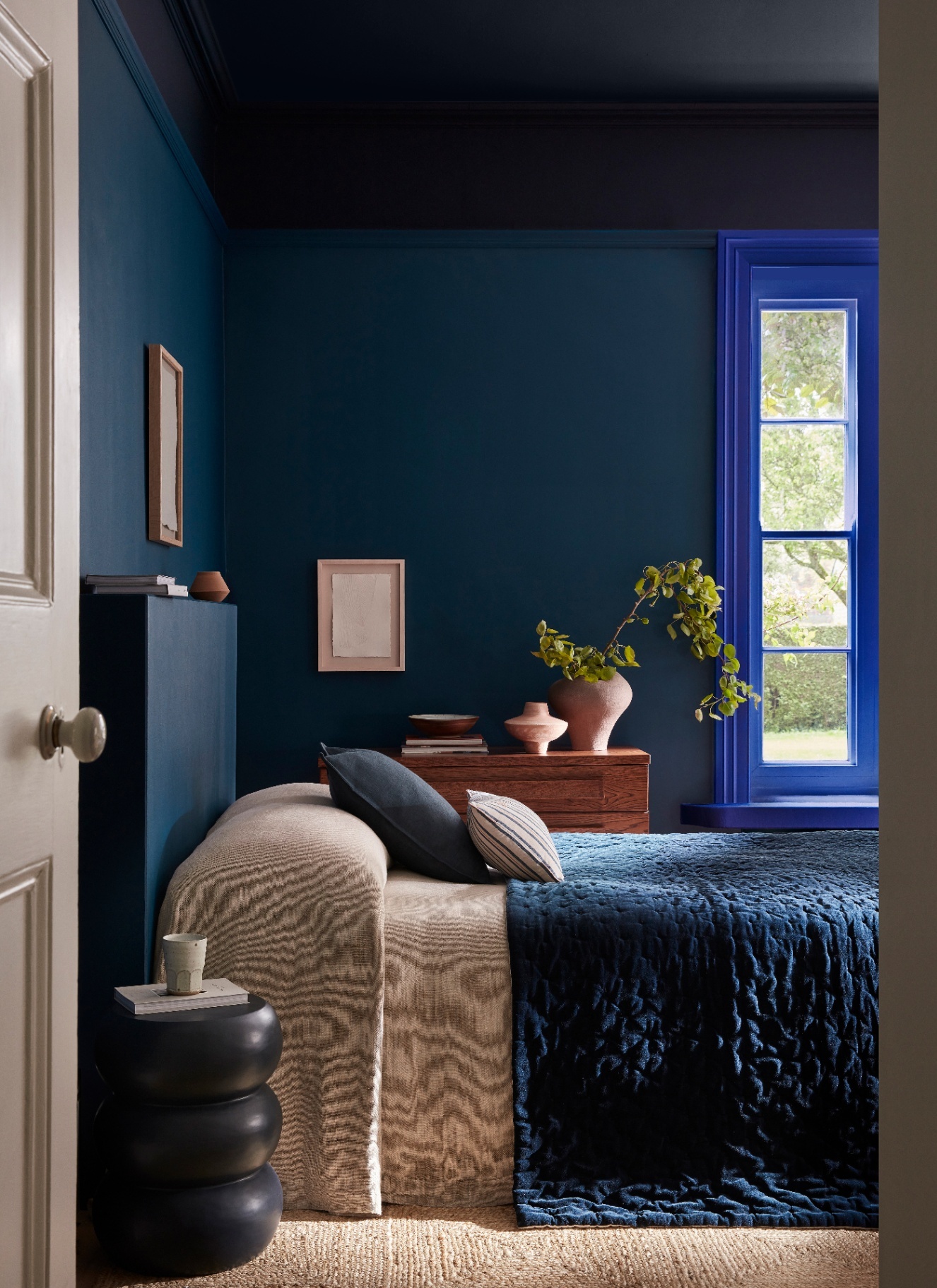 a living room with dark blue colour drenched walls and a bed with beige bedding and a dark blue velvet bedspread