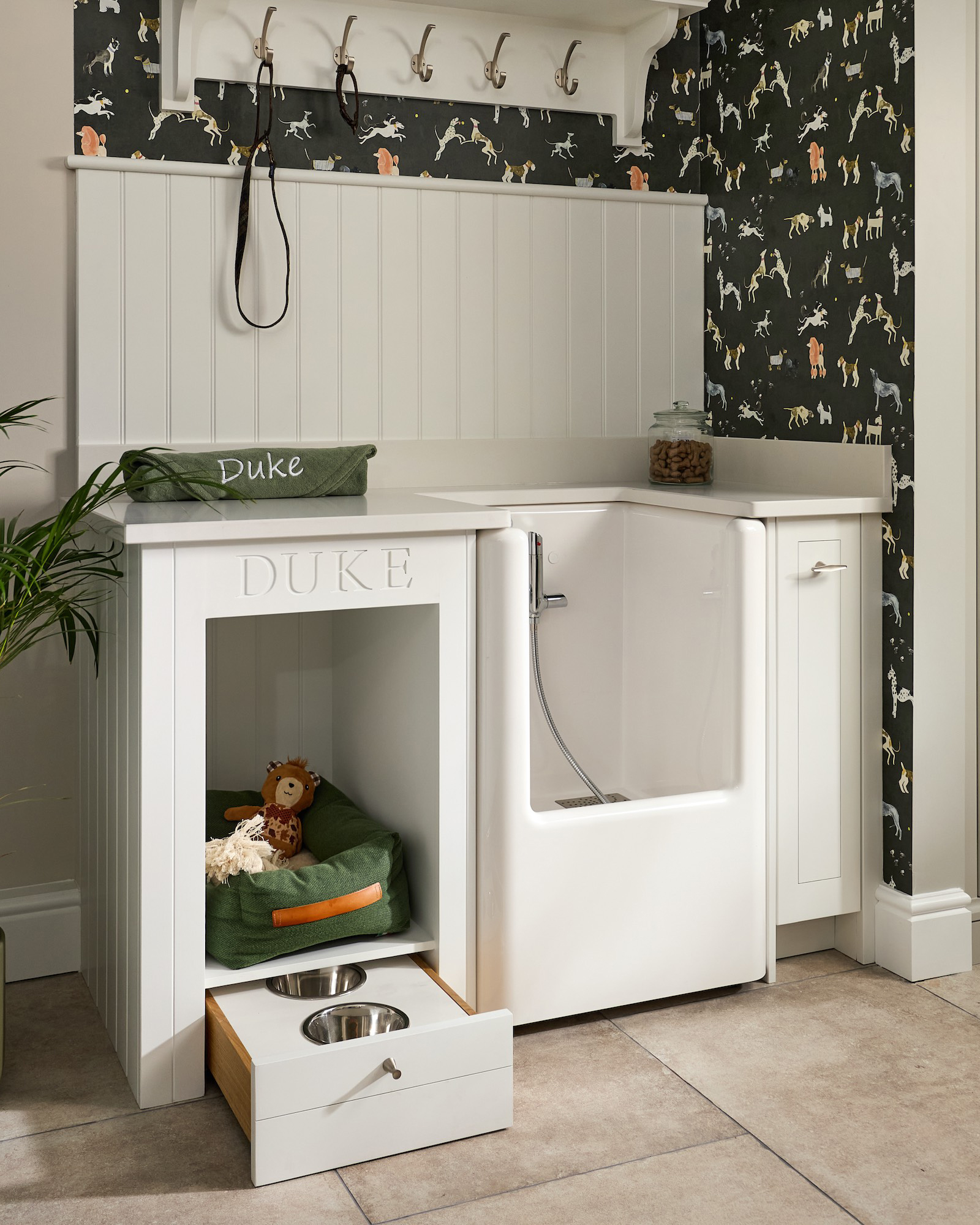 a dog wash station with a built in shower, dark green dog wallpaper and a dog bed alcove with a pull out dog bowl drawer under it