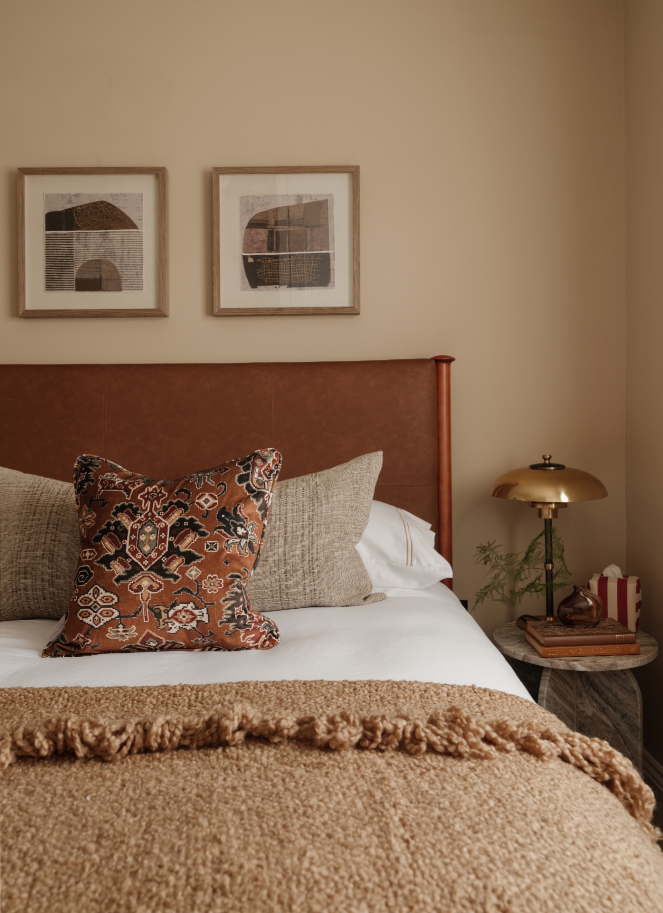 a bedroom with beige walls, a bed with a terracotta headboard and a beige wool throw