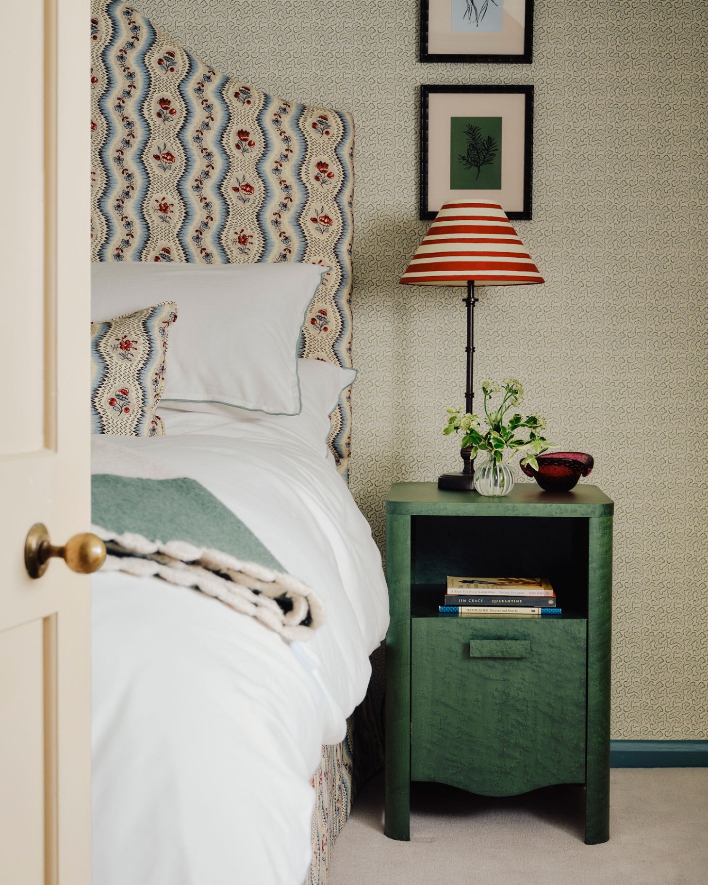 a bedroom with a bed with a blue and white patterned headboard and a green bedside table with a red and white stripe lamp