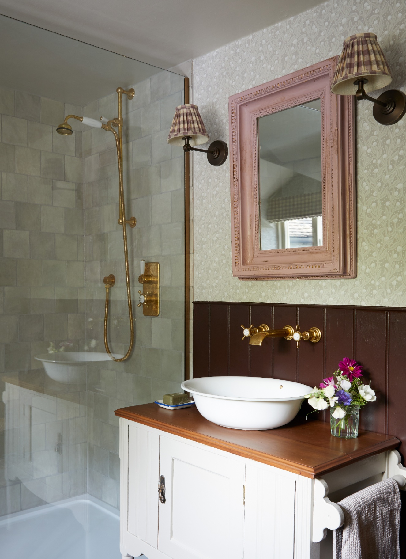 A bathroom with a glass shower door, a white vanity unit, a pink wooden mirror and two pleated gingham wall lights either side