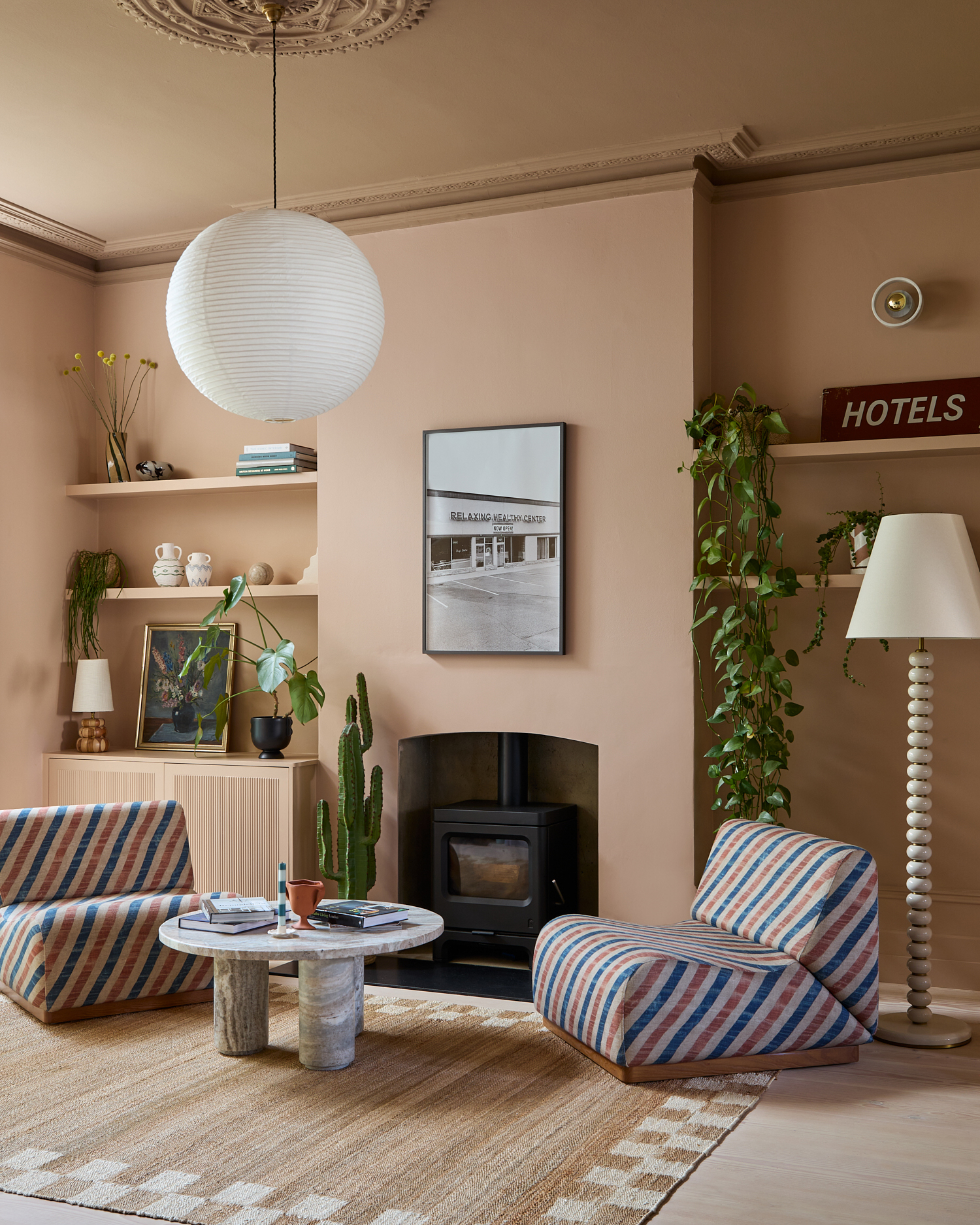 a neutral living room with two large blue, white and red stripe armchairs, a jute rug with a marble coffee table on top and a wood burner with a black and white framed print above it